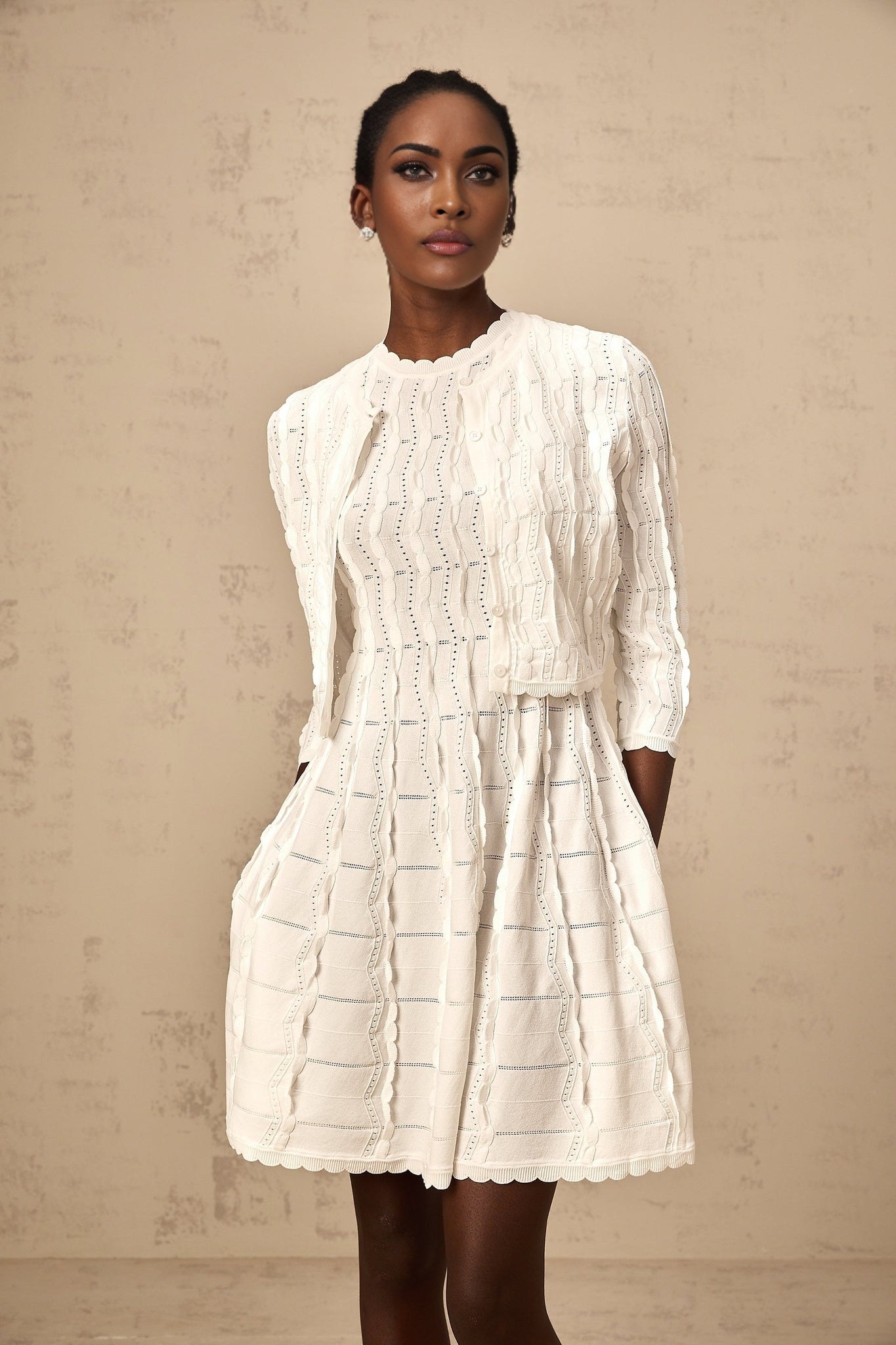 Woman wearing a white knitted cardigan with ruffled details on the front and sleeves