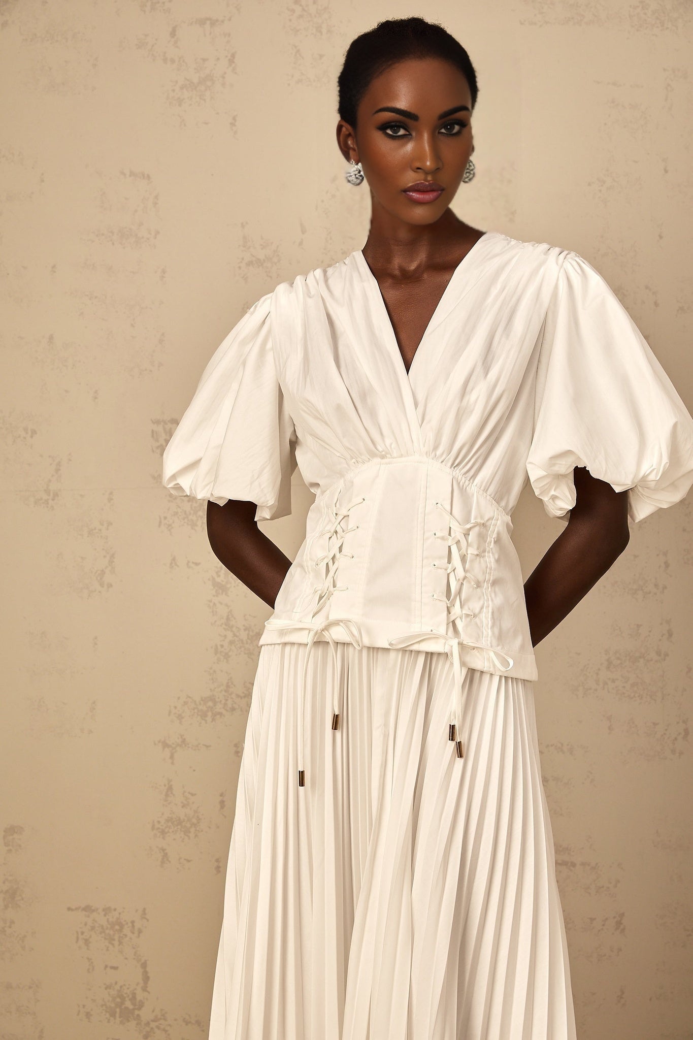 Woman wearing a white lace up maxi dress with pleated details standing in a relaxed pose
