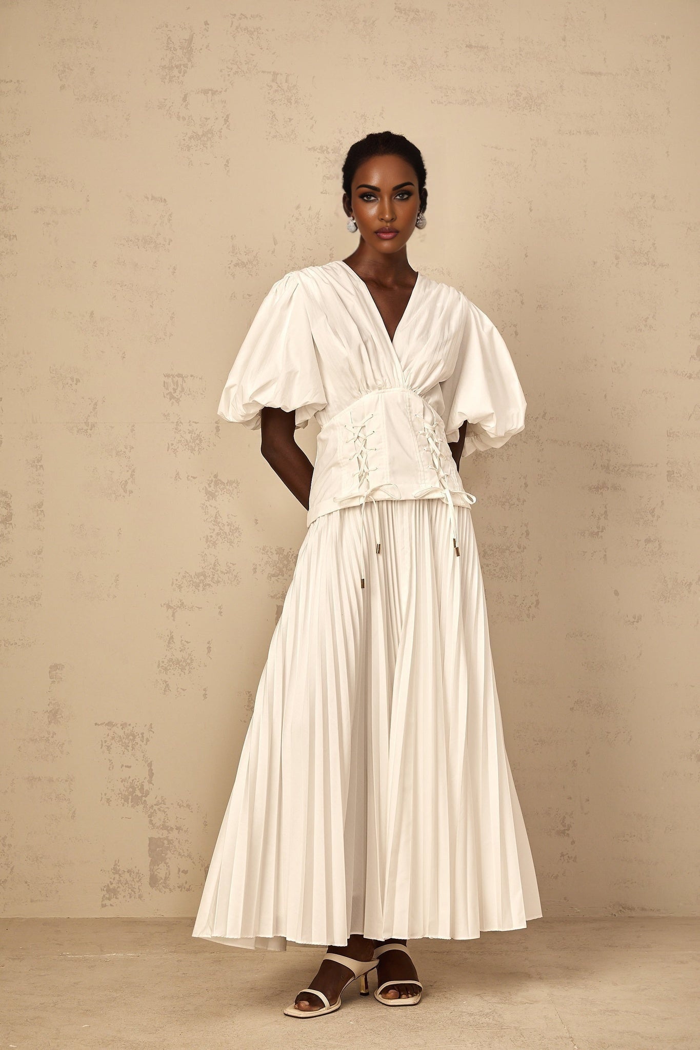 Woman wearing a white lace up pleated maxi dress with long sleeves standing in a relaxed pose