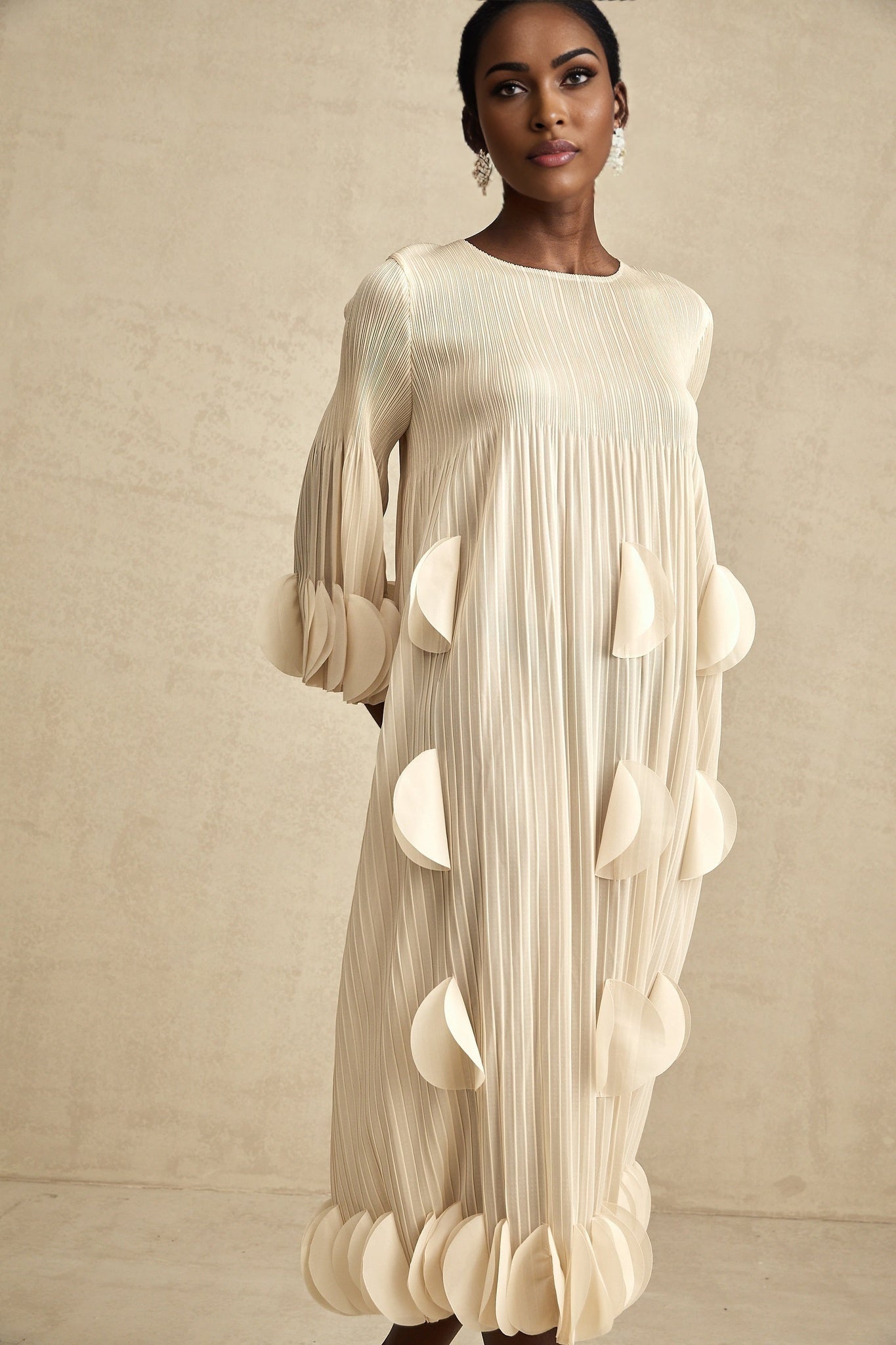 Woman wearing a white midi dress with 3d petal pleated details on the skirt and bodice standing in a neutral setting