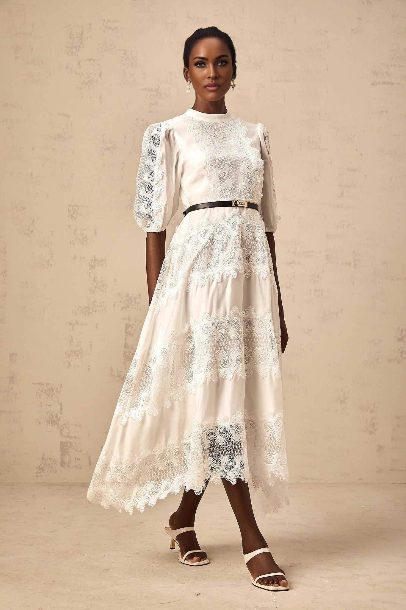 Woman wearing a white midi dress with lace trim panels and belt at waist