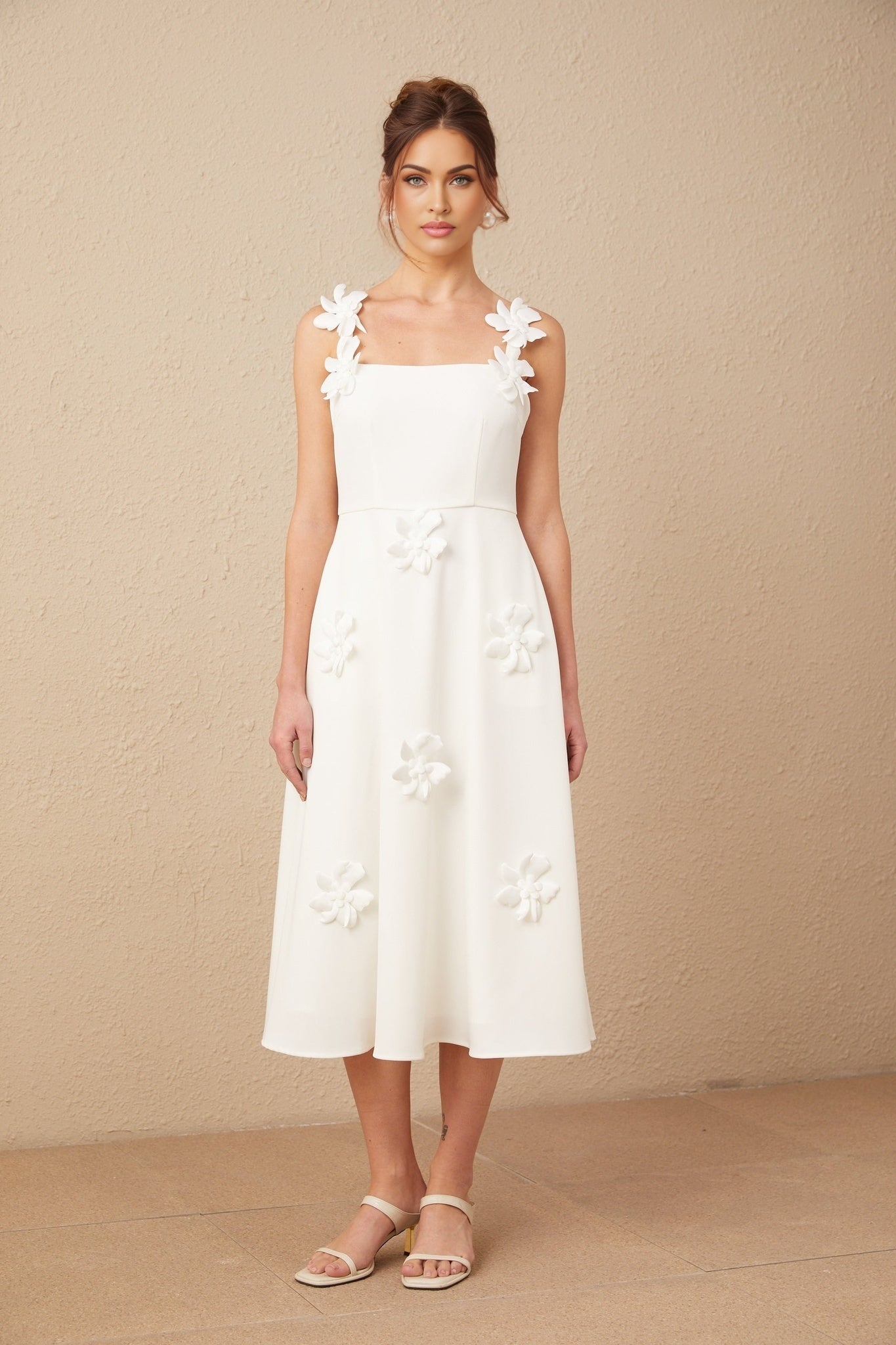Woman wearing a white midi dress with square neckline and floral pattern standing against plain background