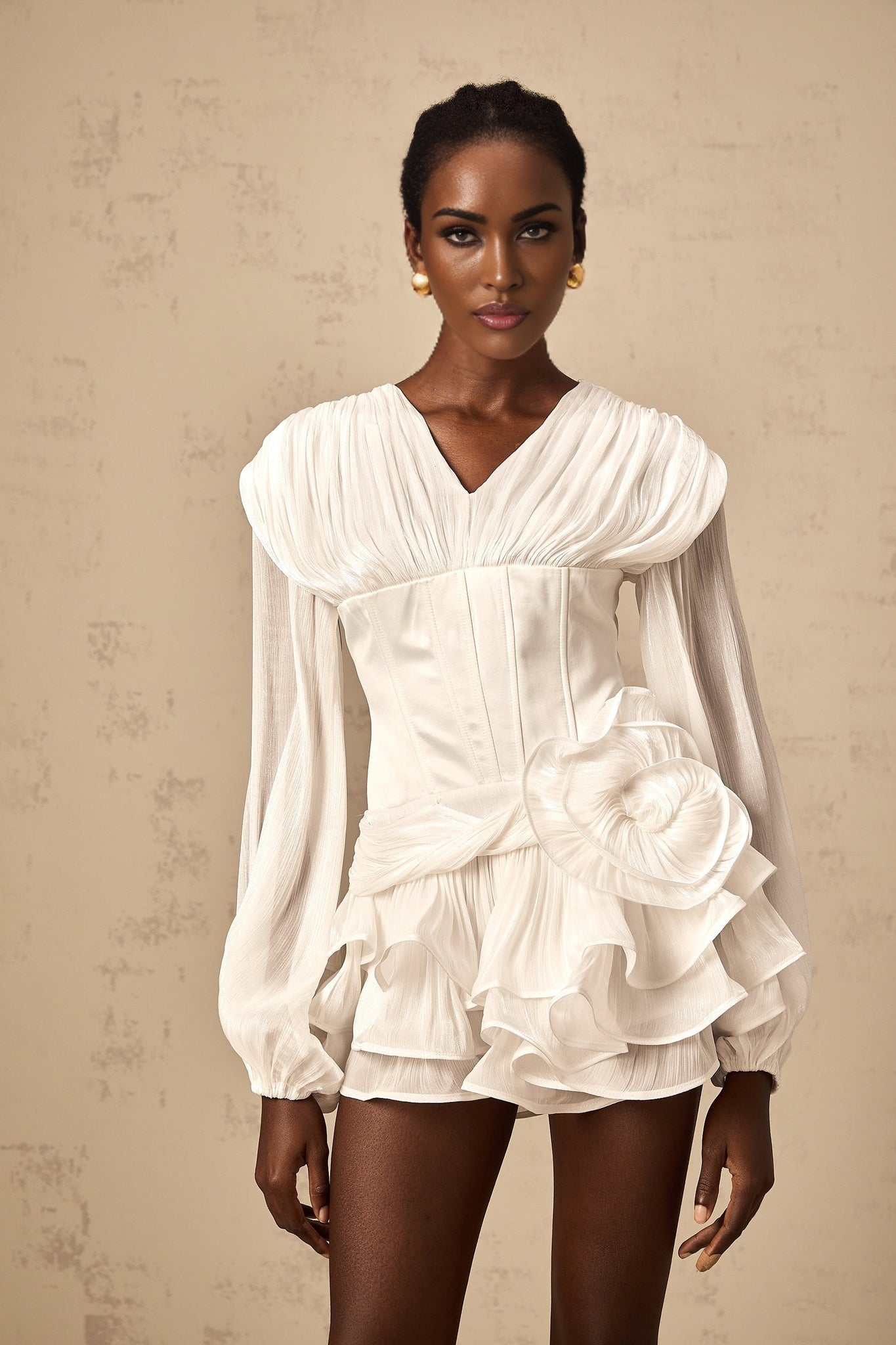 Woman wearing a white mini dress with full pleats and cinched waist detail standing against plain background