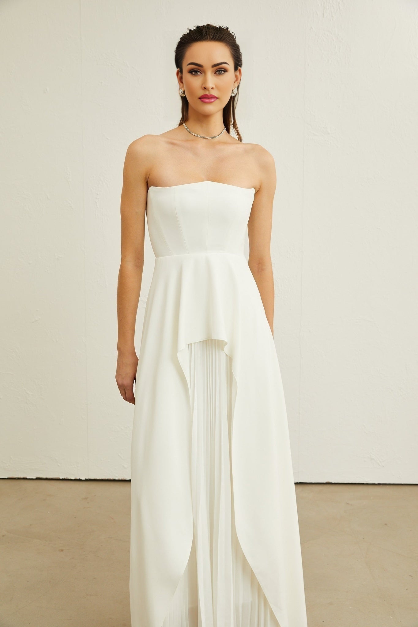 Woman wearing a white pleated off shoulder maxi dress standing in a neutral background