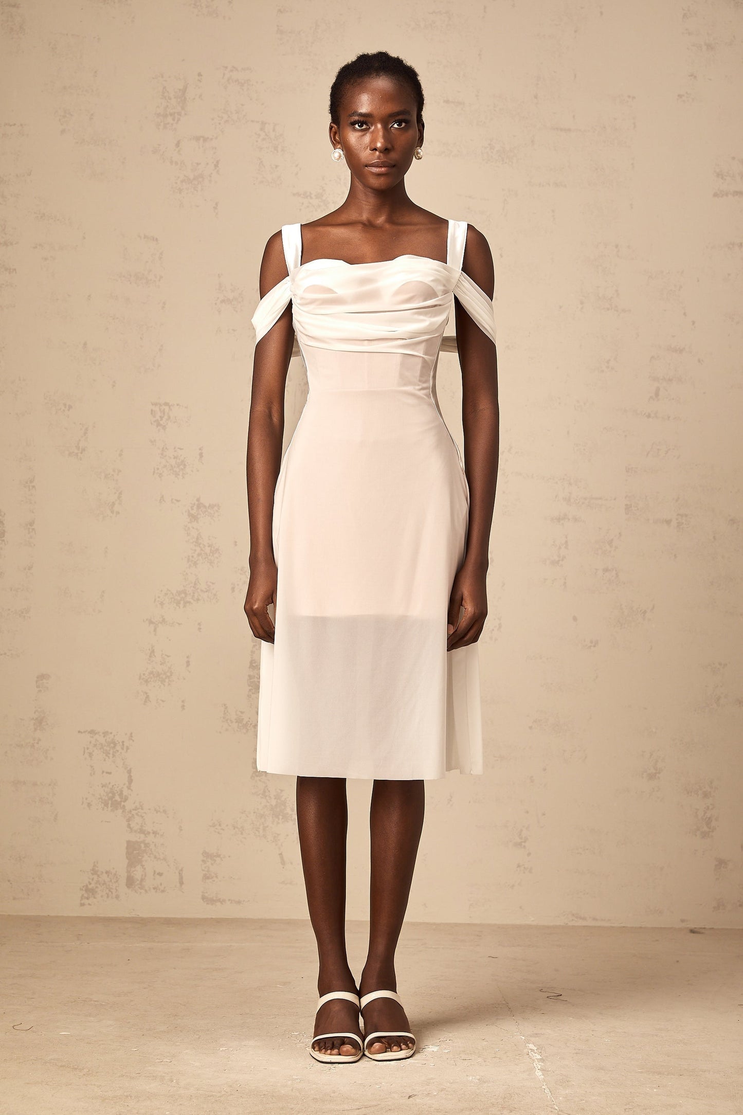 Woman wearing a white semi sheer ruched midi dress with gathered fabric details standing in a relaxed pose