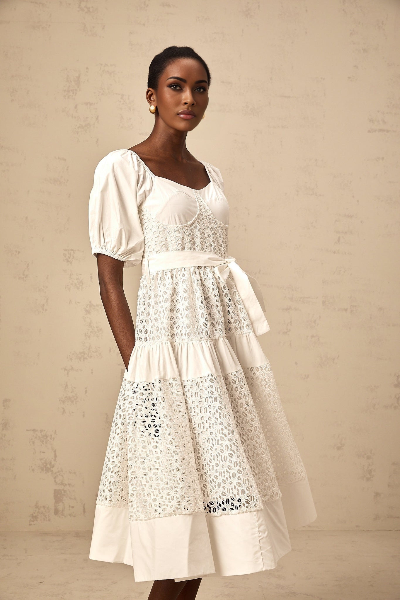 Woman wearing a white tiered midi dress made of corded lace named Helene standing in a neutral background