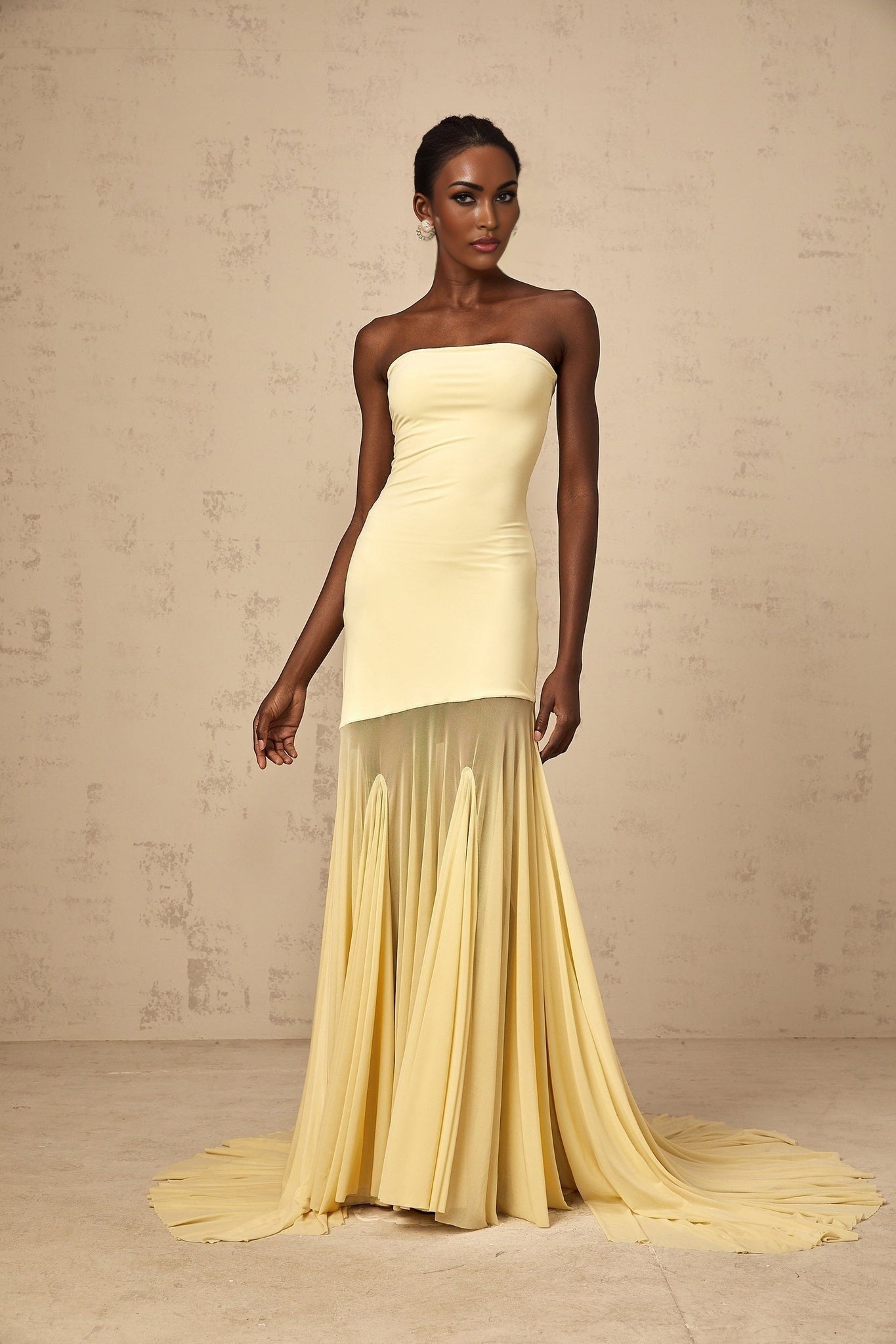 Woman wearing a yellow off shoulder maxi dress with sheer tulle fabric standing against a plain background
