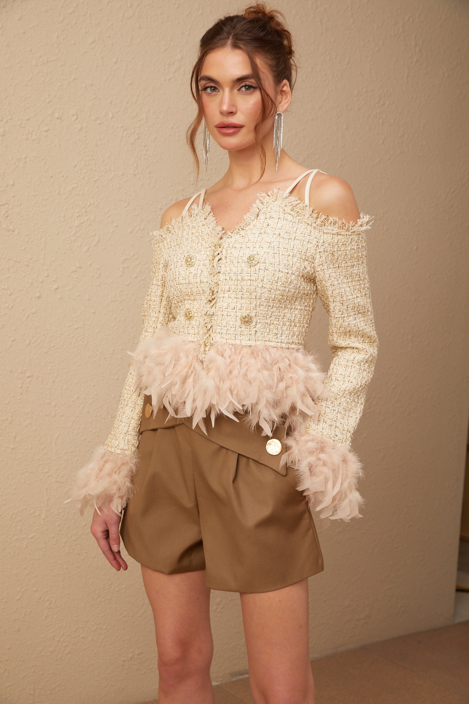Woman wearing an offshoulder tweed top with feather trim along the neckline in a light colored fabric