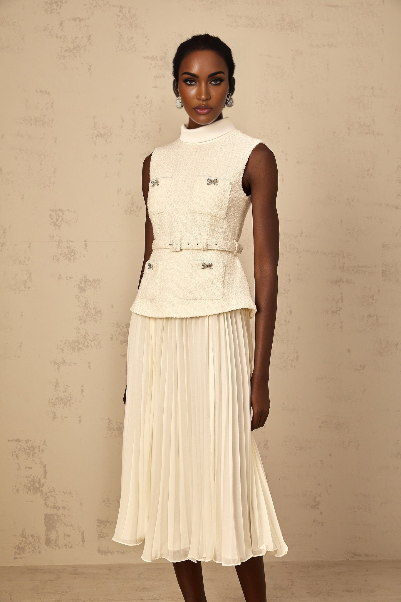 Woman wearing an offwhite midi dress with tweed fabric and tulle panel details standing in a neutral background