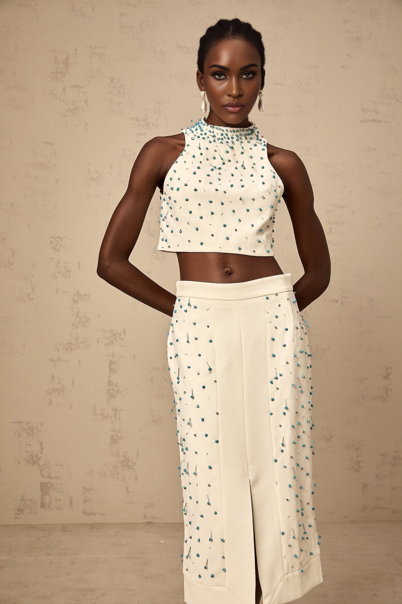 Woman wearing an offwhite two piece outfit consisting of an embellished top and matching skirt