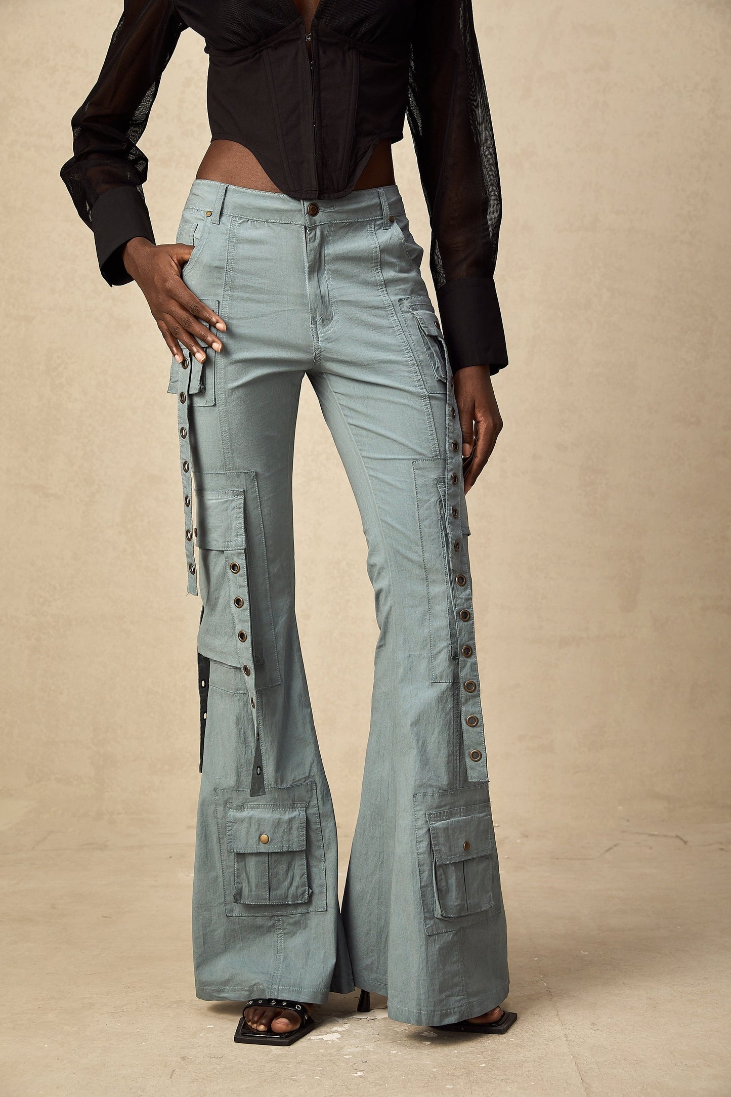 Woman wearing beige flared cargo trousers with belt loops and multiple pockets standing in casual pose