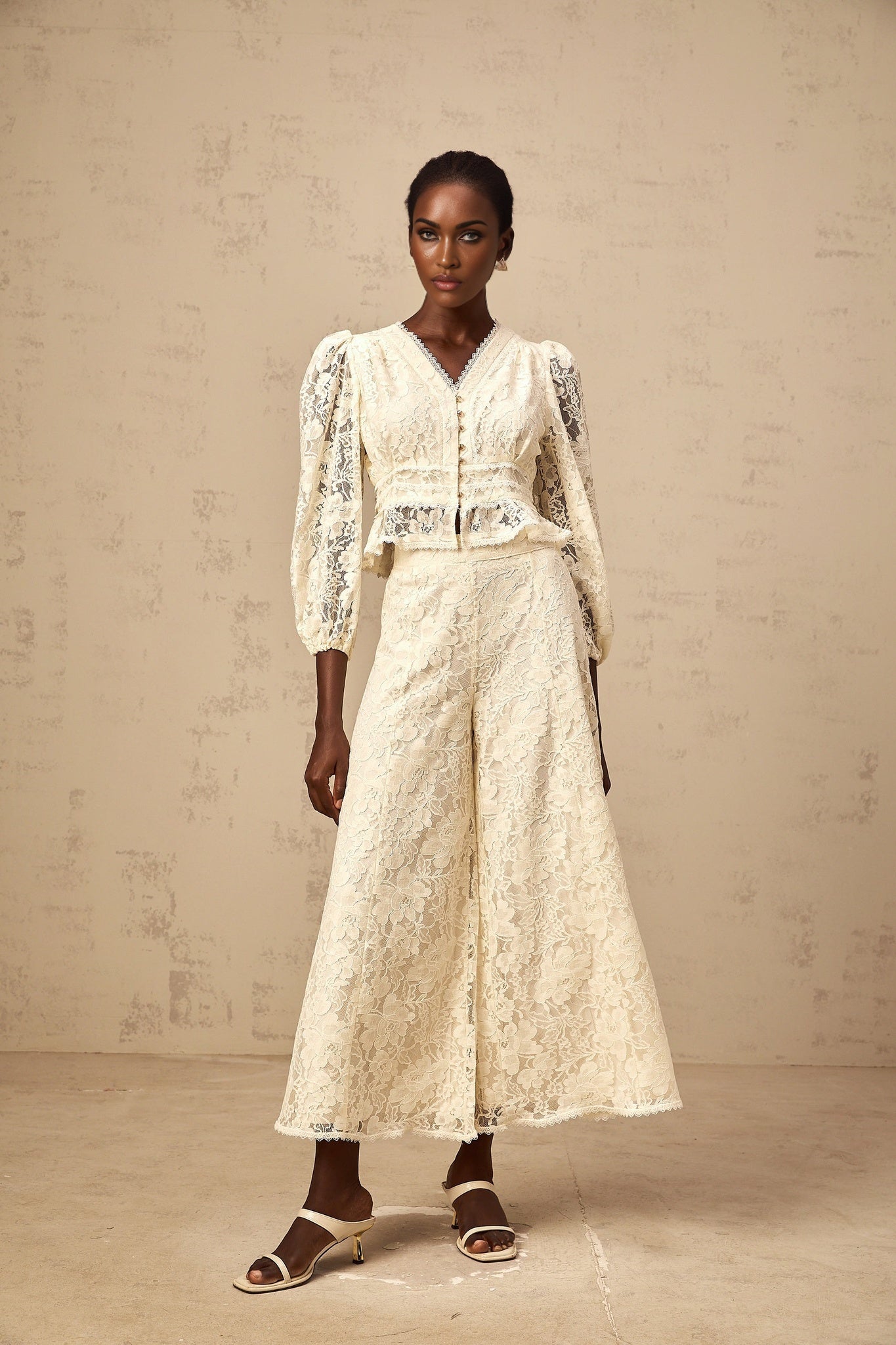 Woman wearing beige floral lace blouse and matching trousers set with delicate pattern and neutral color scheme