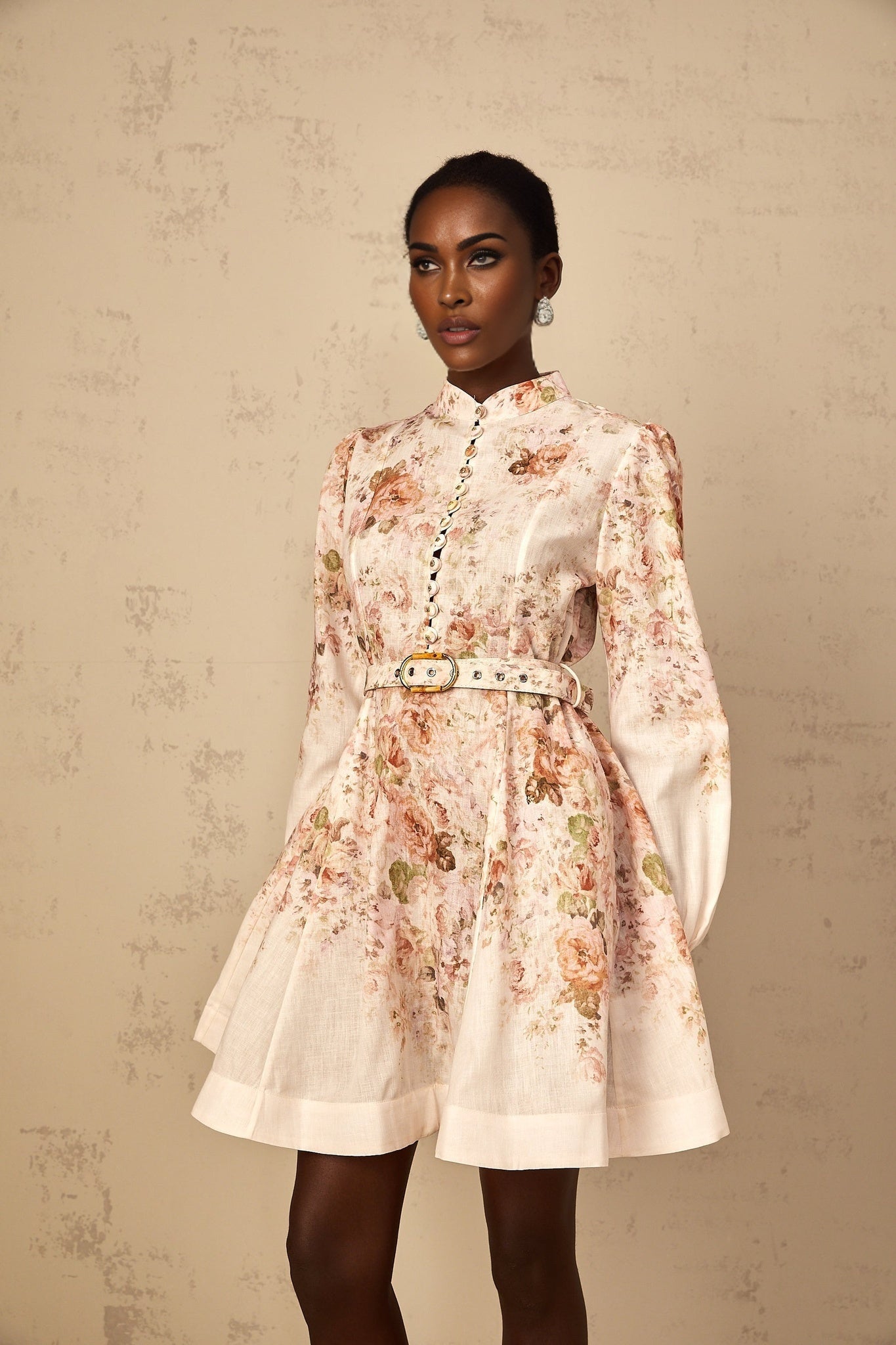 Woman wearing beige mini dress with floral print standing against plain background