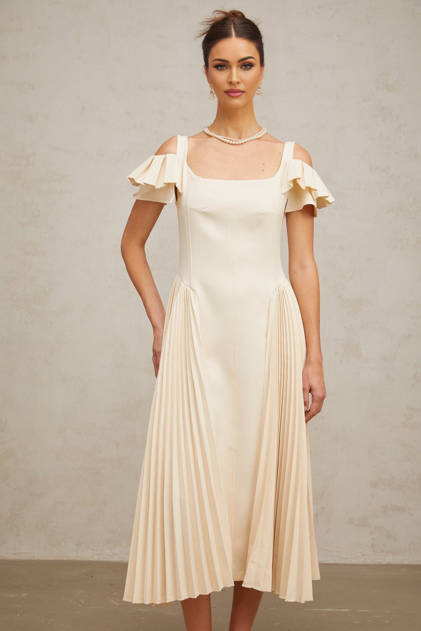 Woman wearing beige pleated midi dress with flared skirt and neutral tones standing in elegant pose