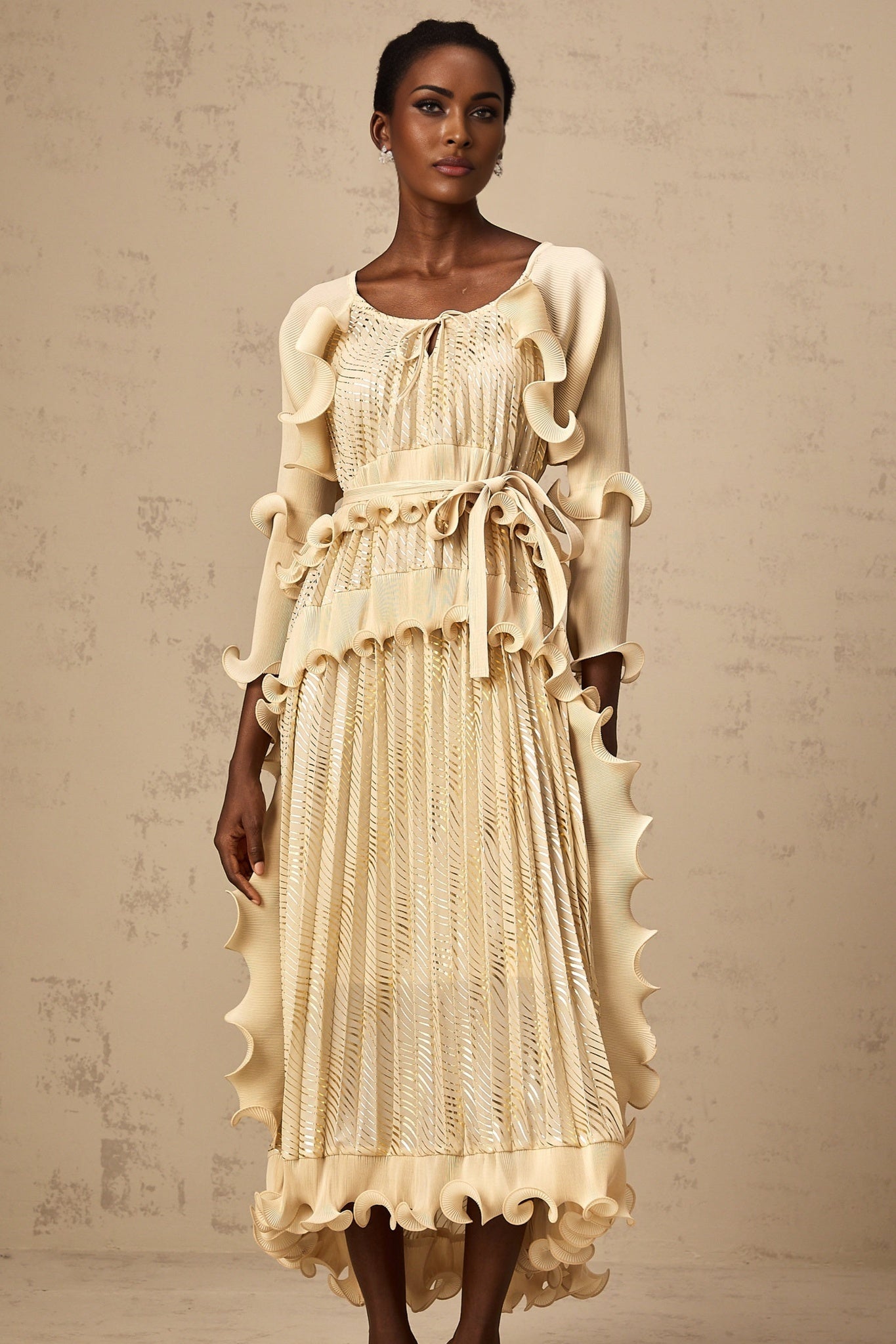 Woman wearing beige ruffled midi dress with gilded details standing in neutral pose
