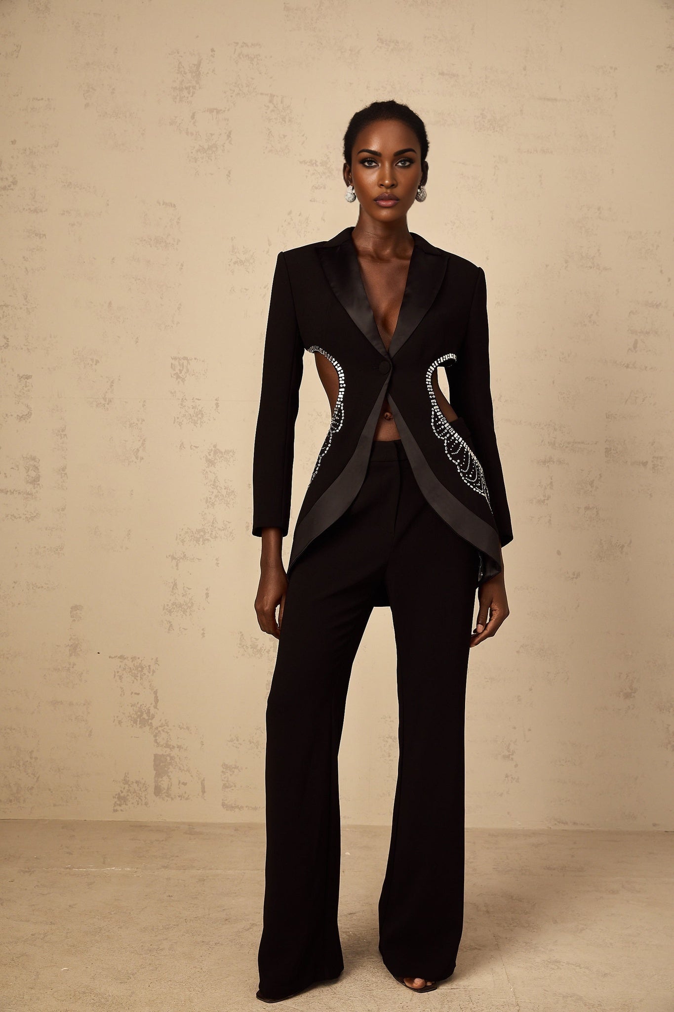 Woman wearing black blazer and trousers set with cutout details and embellishments