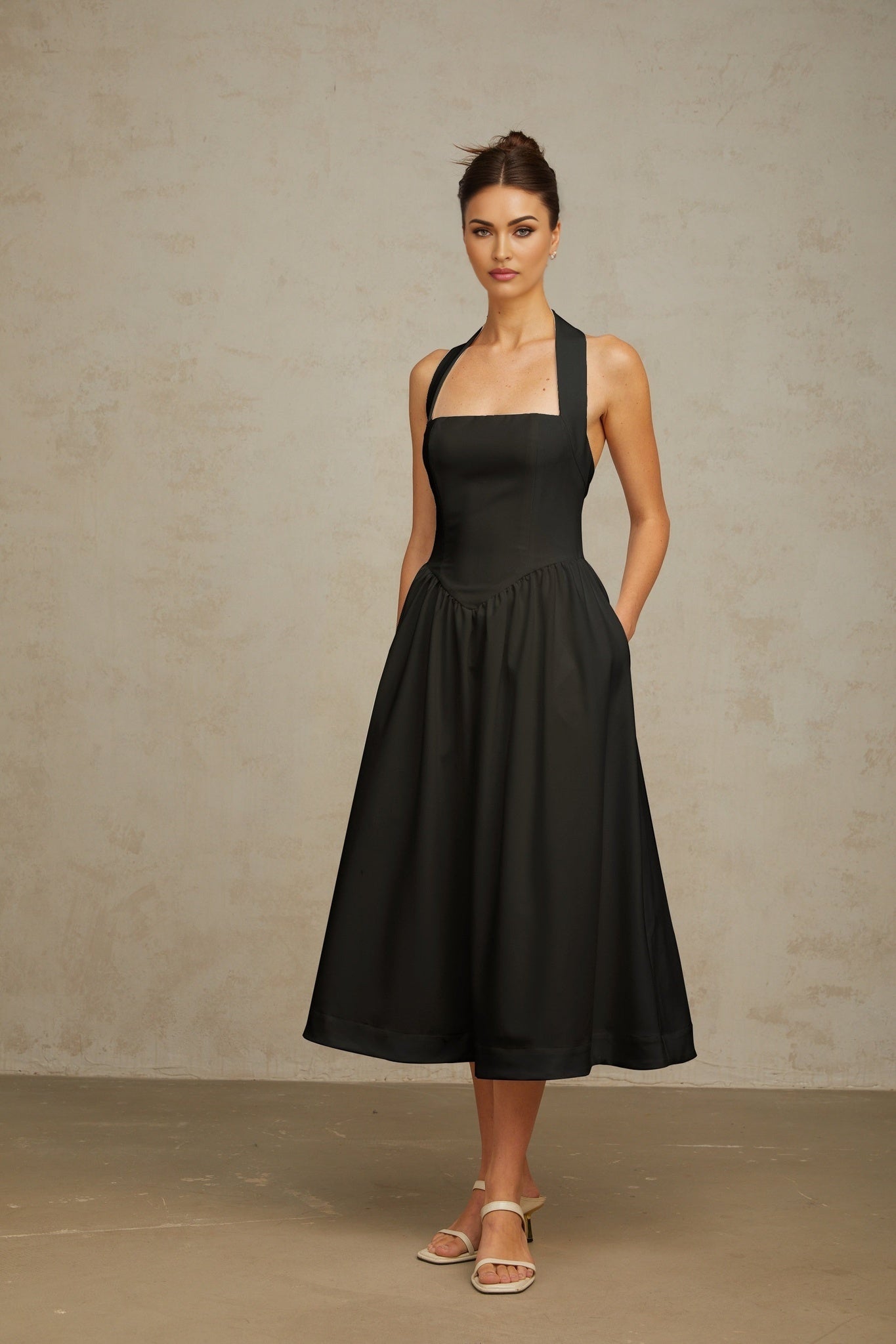 Woman wearing black halterneck pleated midi dress with fitted waist and flared skirt