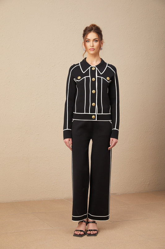 Woman wearing black jacket and trousers with white piping detail matching set