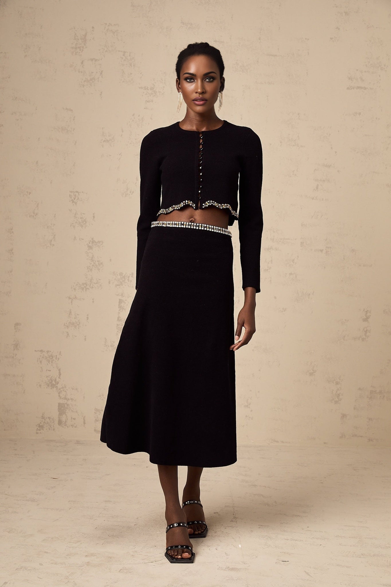 Woman wearing black knitted cardigan and matching skirt set with embellishments