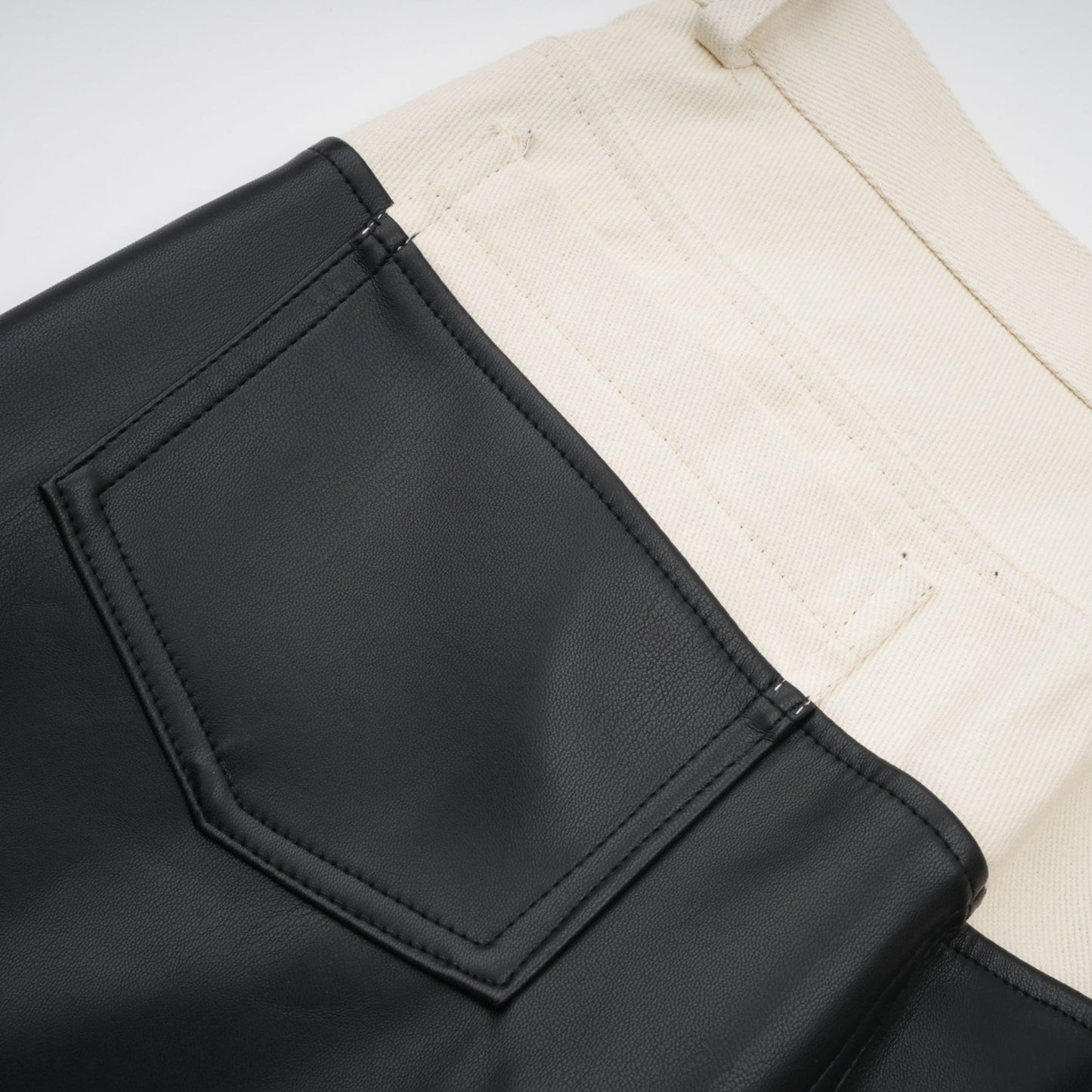 Woman wearing black leather trousers with white contrast panels on the sides standing in a neutral pose