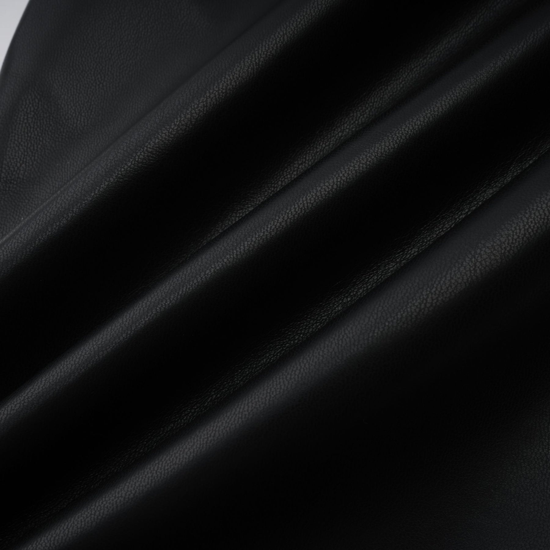 Woman wearing black leather trousers with white contrast stitching and side panels standing against a plain background