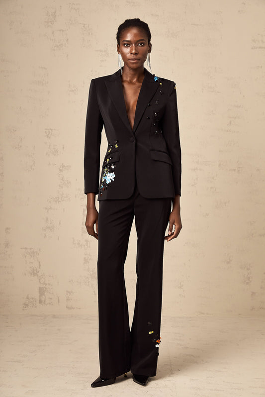 Woman wearing black sequined blazer and matching trousers standing against plain background