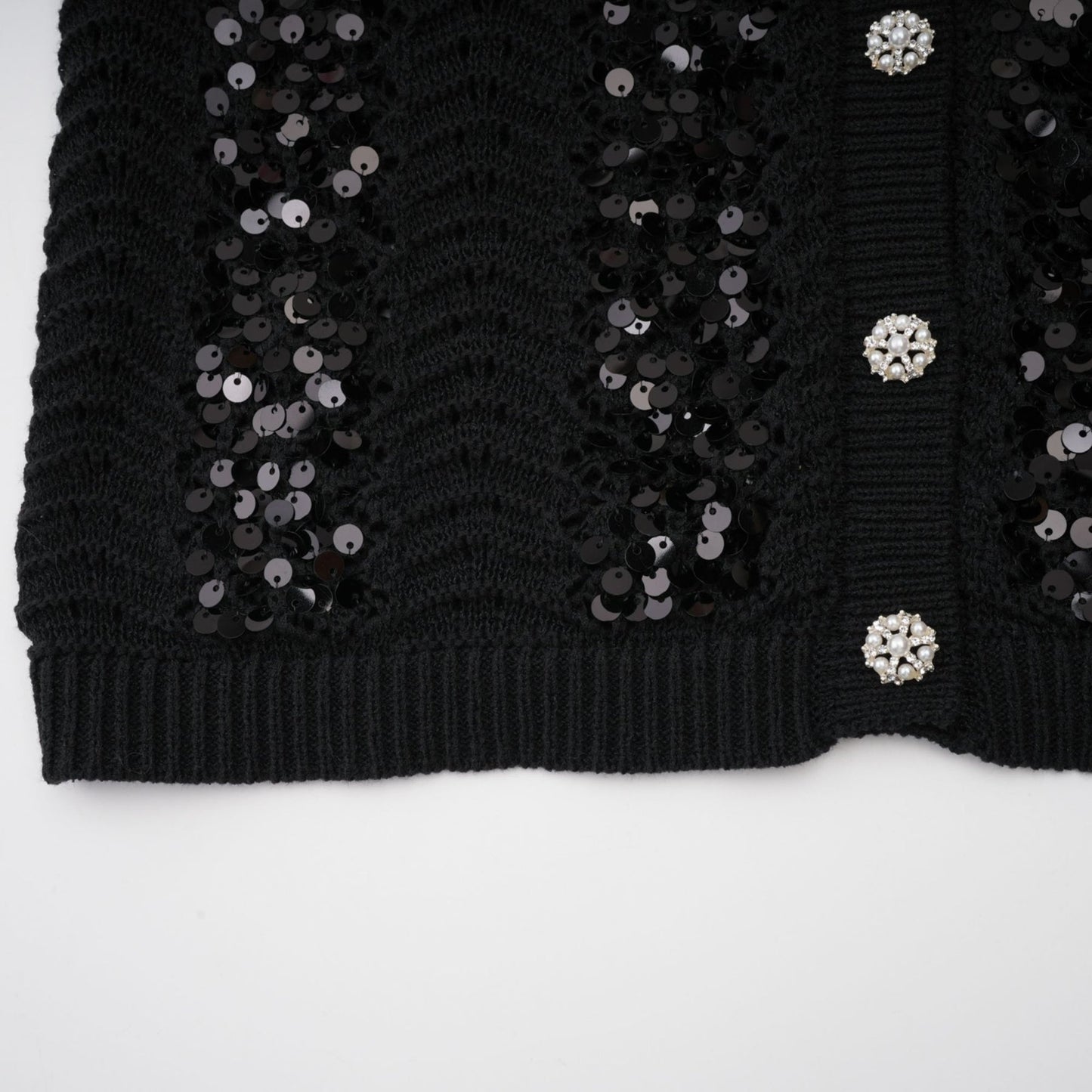 Woman wearing black sequined crochet knit cardigan and matching skirt set against plain background