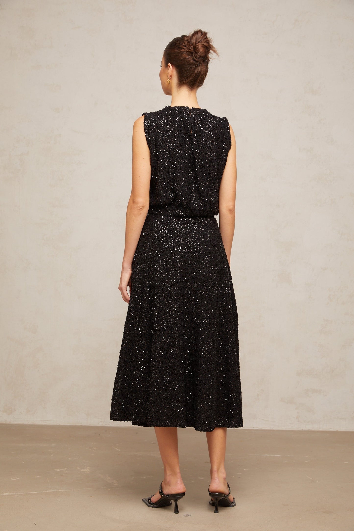 Woman wearing black sequined knit vest and matching skirt set Ulrique outfit shimmering sleeveless top with coordinating bottom
