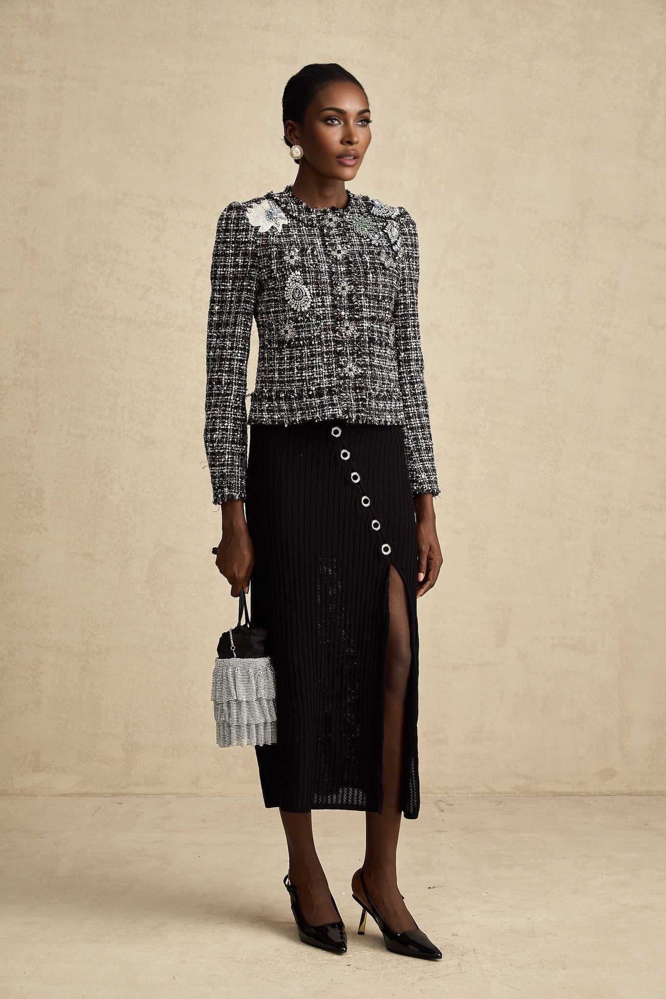 Woman wearing black tweed jacket with frayed edges and subtle check pattern Standing against plain background