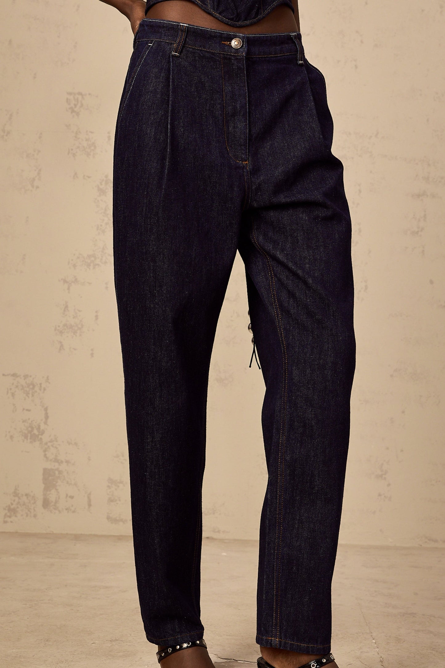 Woman wearing blue high rise jeans with pleated details on the front standing in a casual pose