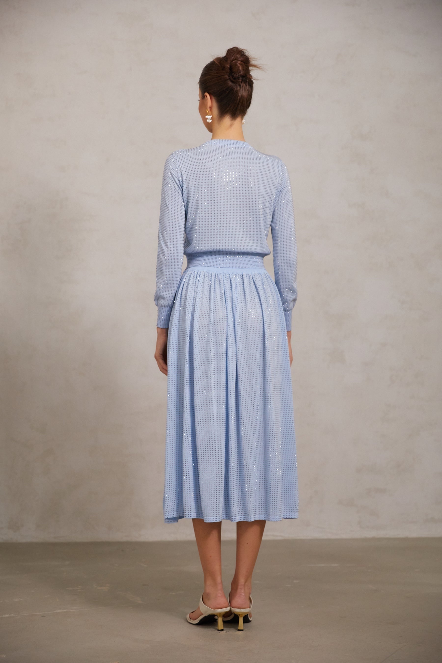 Woman wearing blue knitted top and matching skirt adorned with rhinestone embellishments
