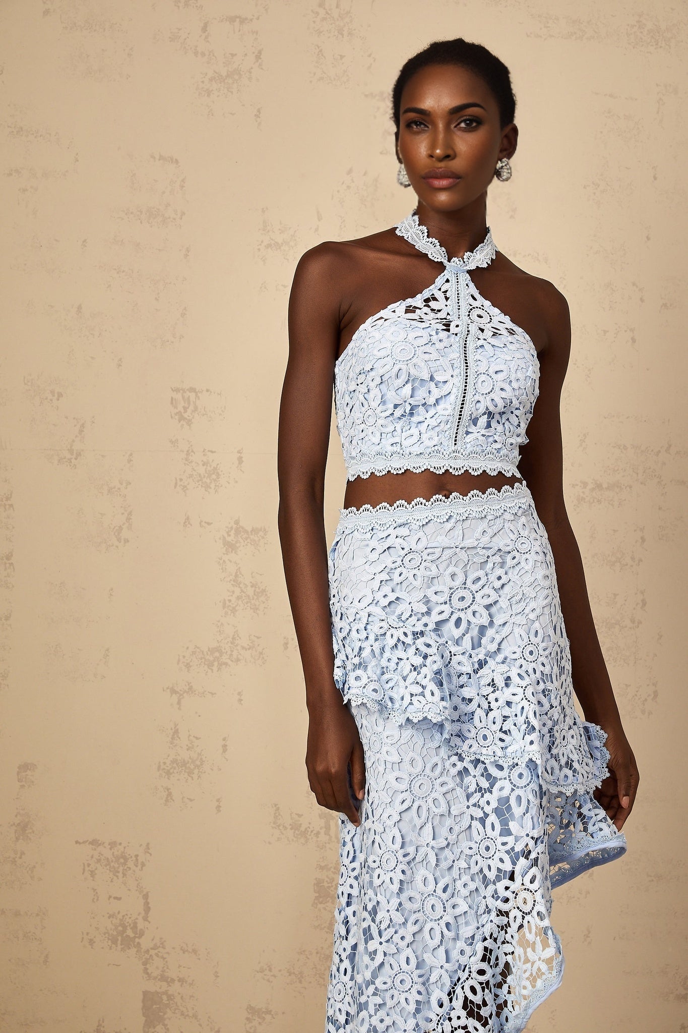Woman wearing blue lace top and matching bottoms set against plain background
