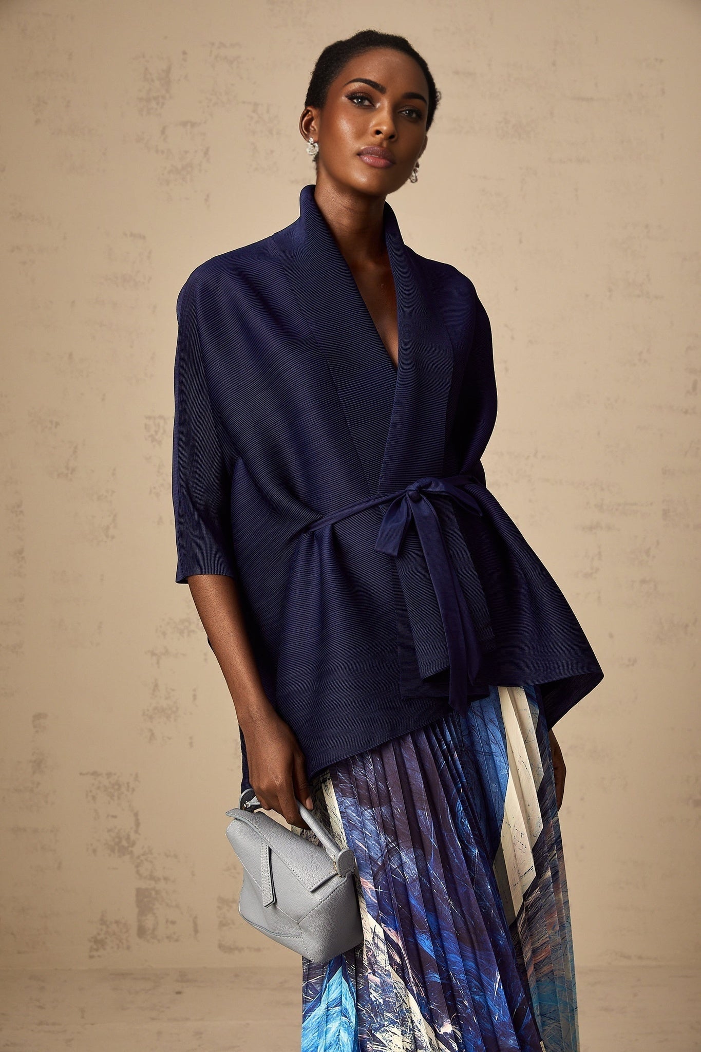 Woman wearing blue patterned cape and matching skirt set against plain background