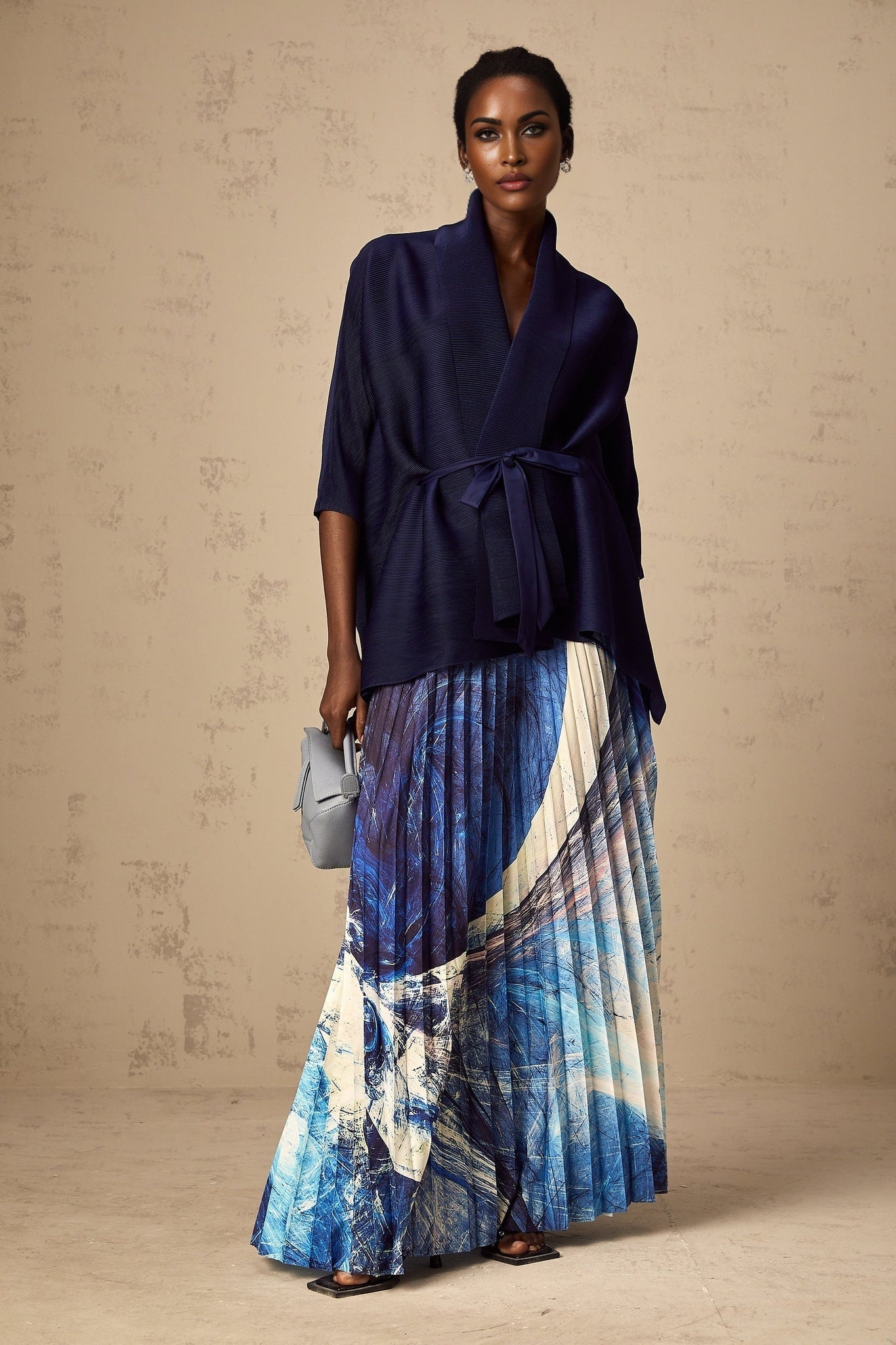 Woman wearing blue patterned cape and matching skirt set with crease detailing and allover print design