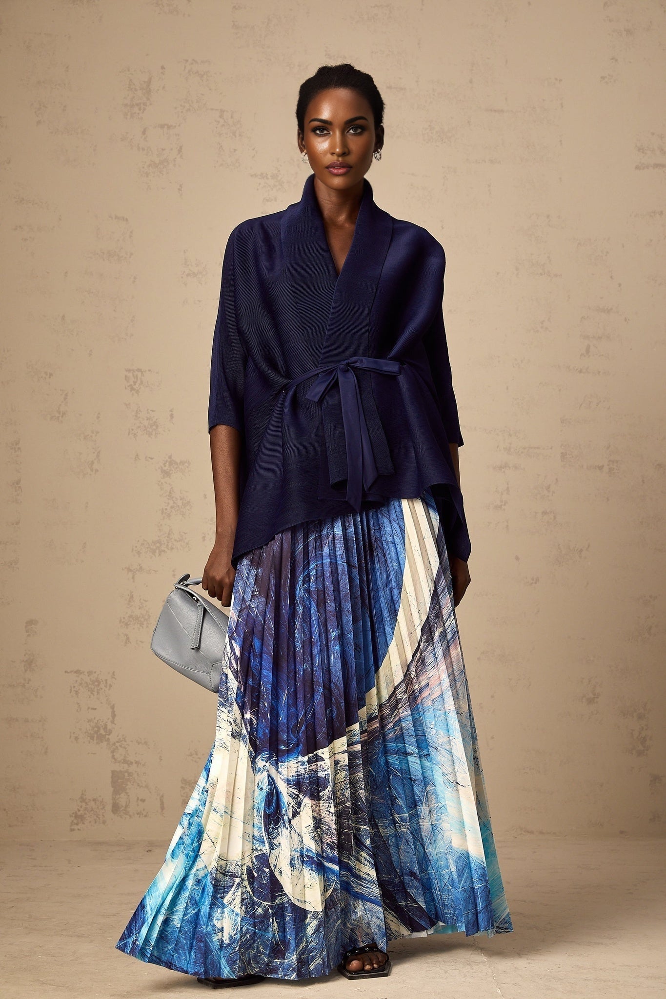 Woman wearing blue patterned cape and matching skirt set with crease details and allover print design