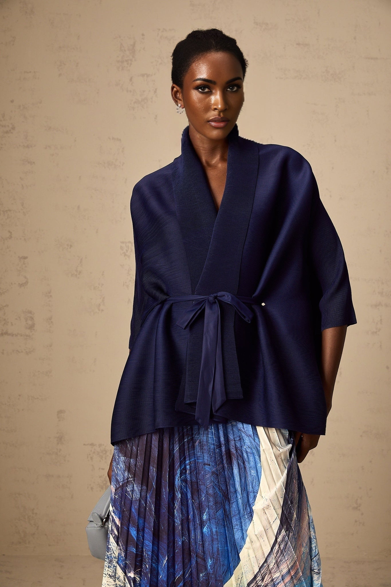 Woman wearing blue patterned cape and matching skirt set with creased fabric design