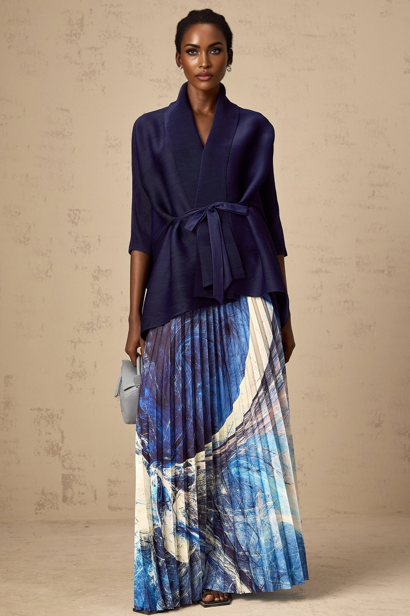 Woman wearing blue patterned cape and matching skirt set with creased texture Standing against plain background
