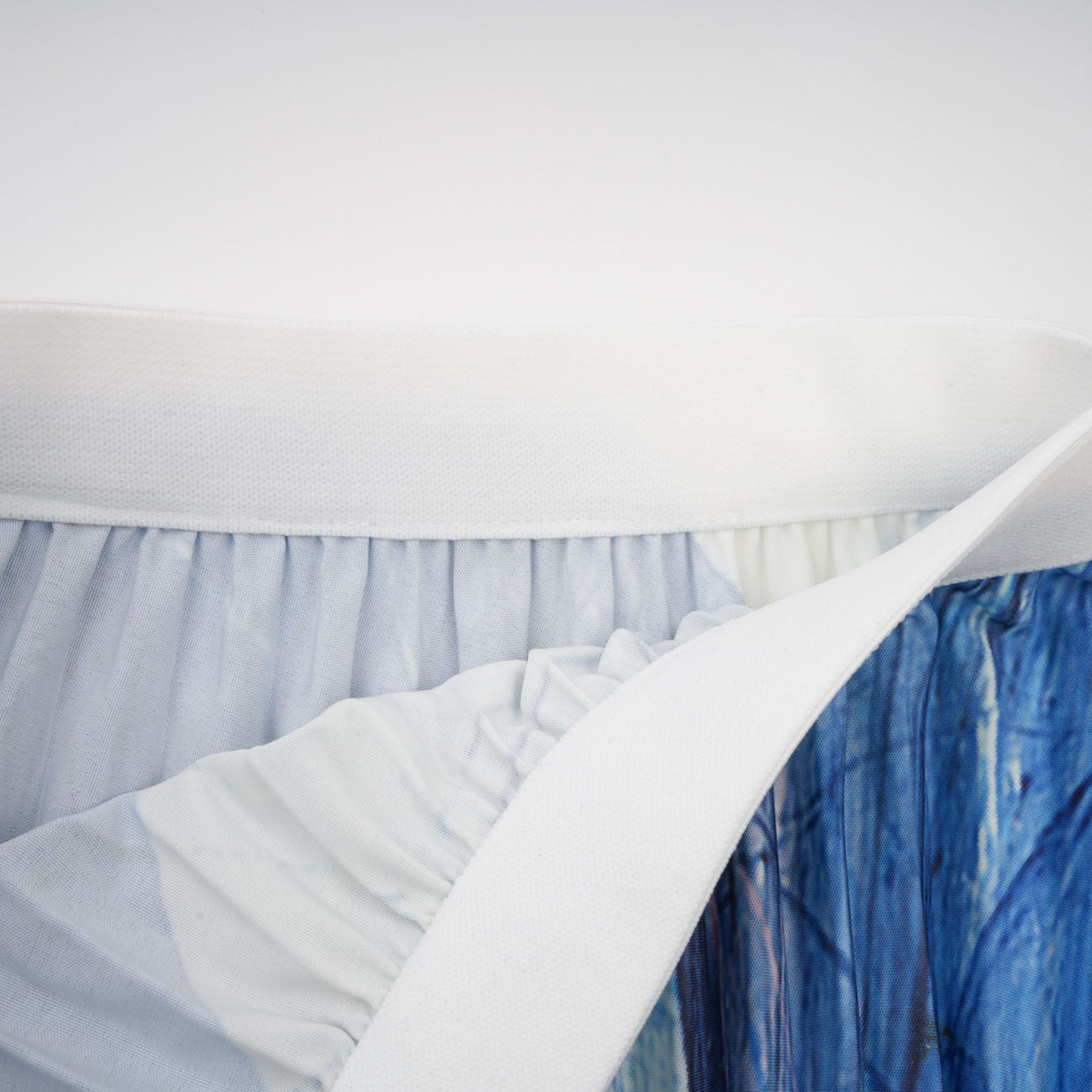 Woman wearing blue patterned cape and matching skirt set with crinkled fabric texture standing against plain background