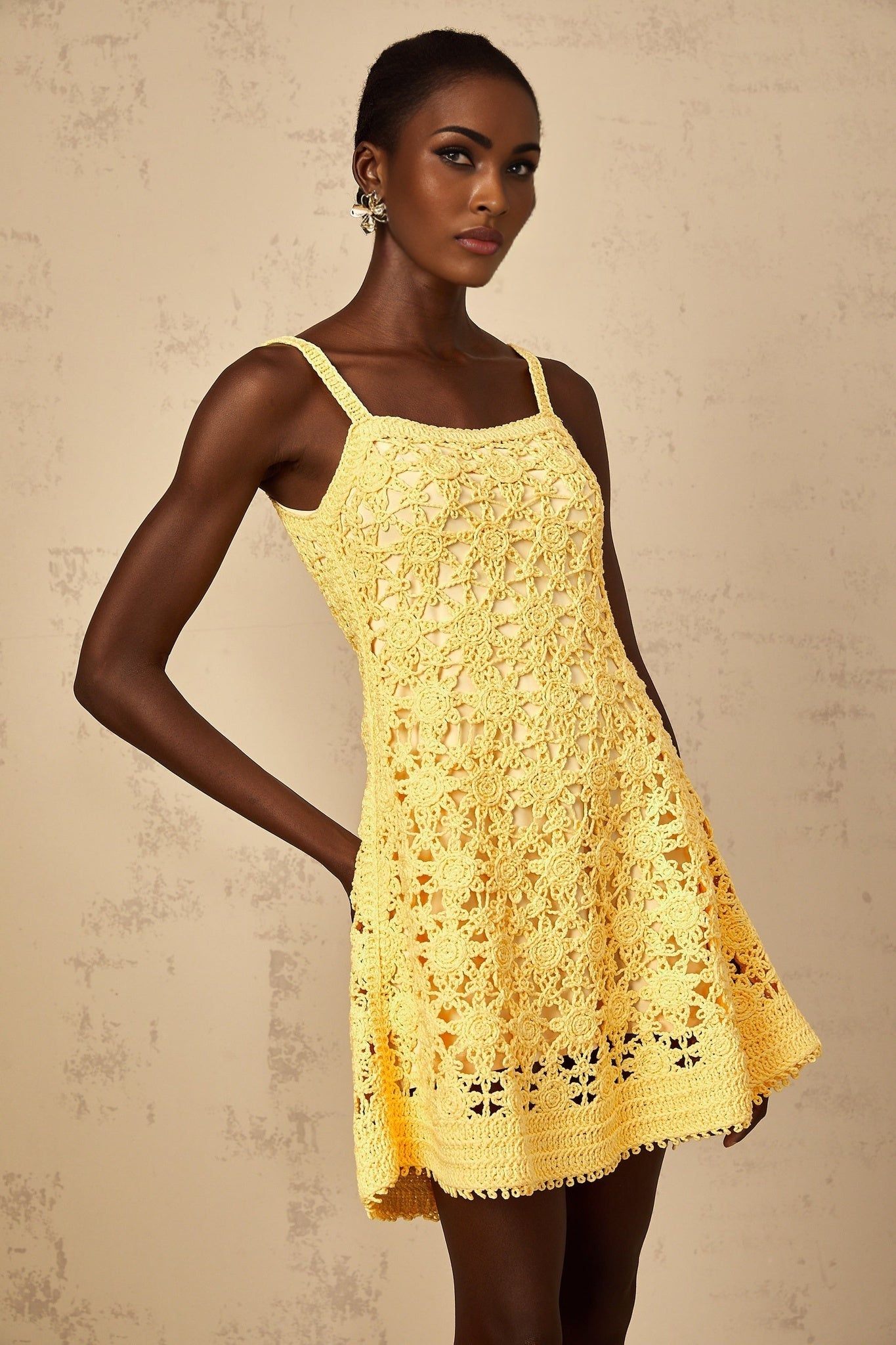 Woman wearing bright yellow crochet knit mini dress with flared skirt standing against plain background