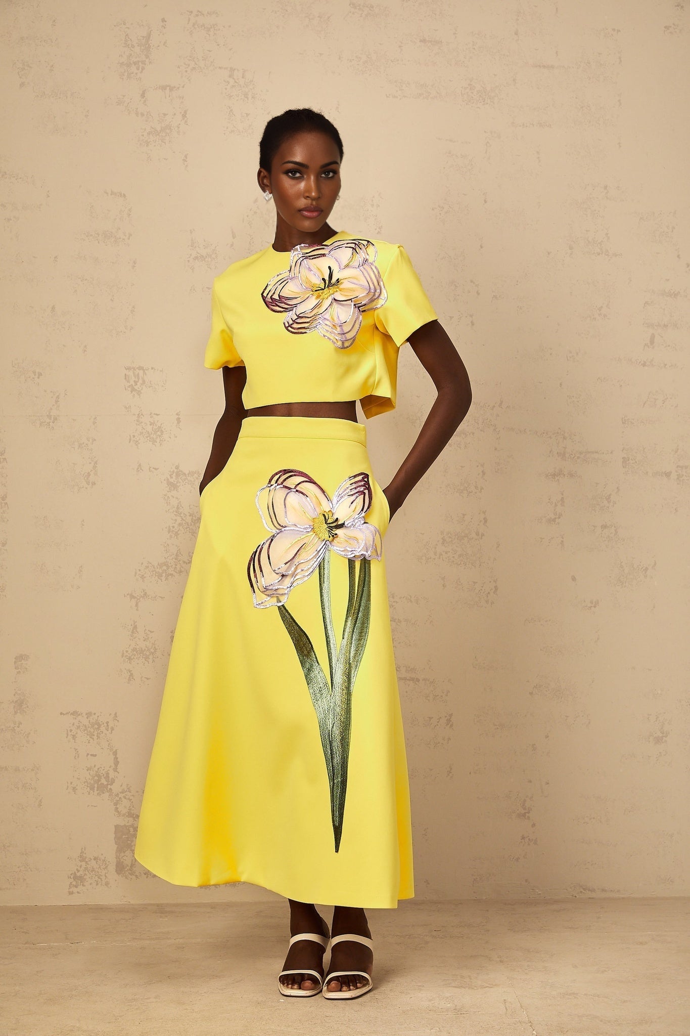 Woman wearing bright yellow two piece outfit with sequin floral embroidery top and matching bottoms
