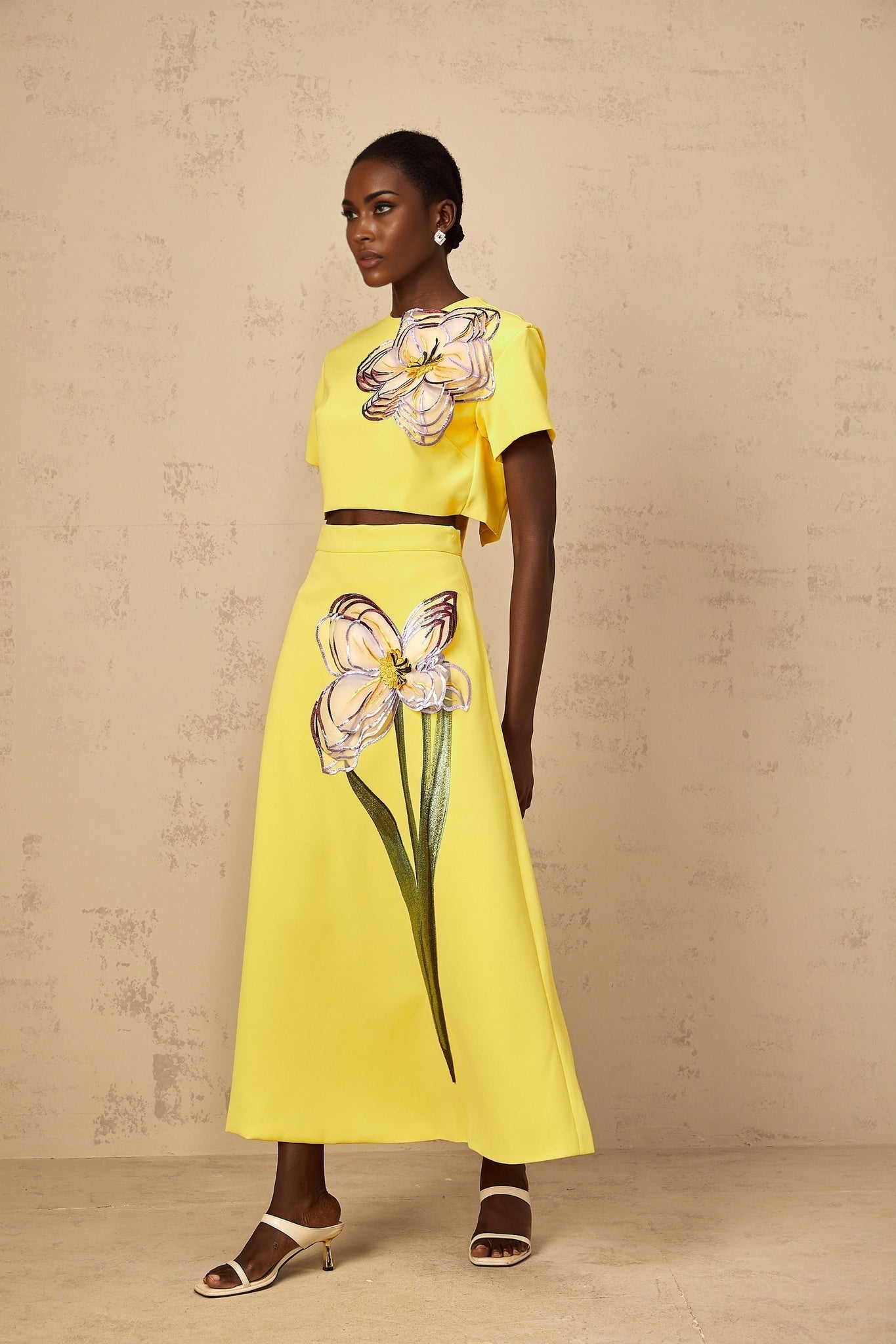 Woman wearing bright yellow twopiece outfit with sequin floral embroidery top and matching bottoms
