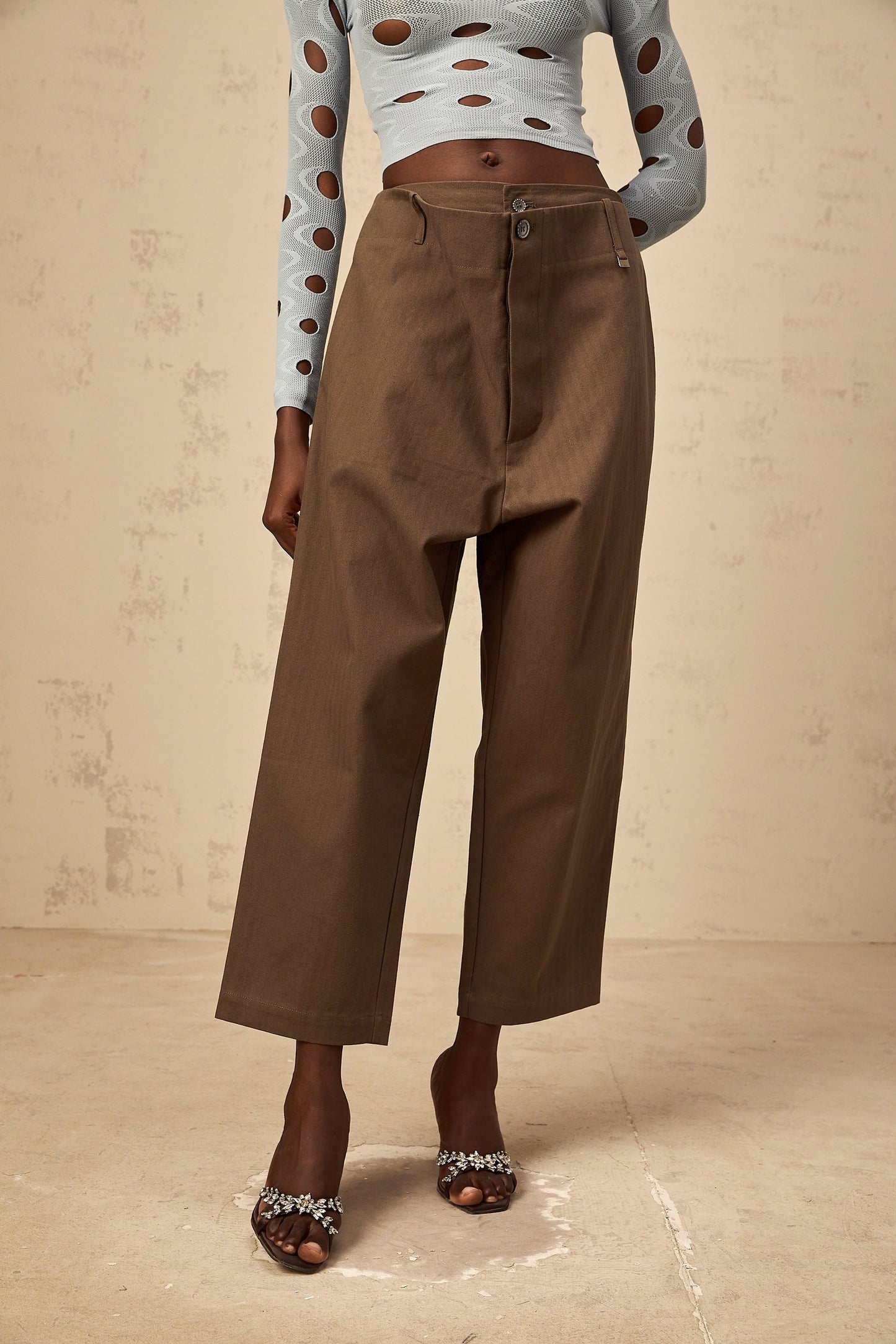 Woman wearing brown wide leg cropped trousers with shirred waistband standing against neutral background