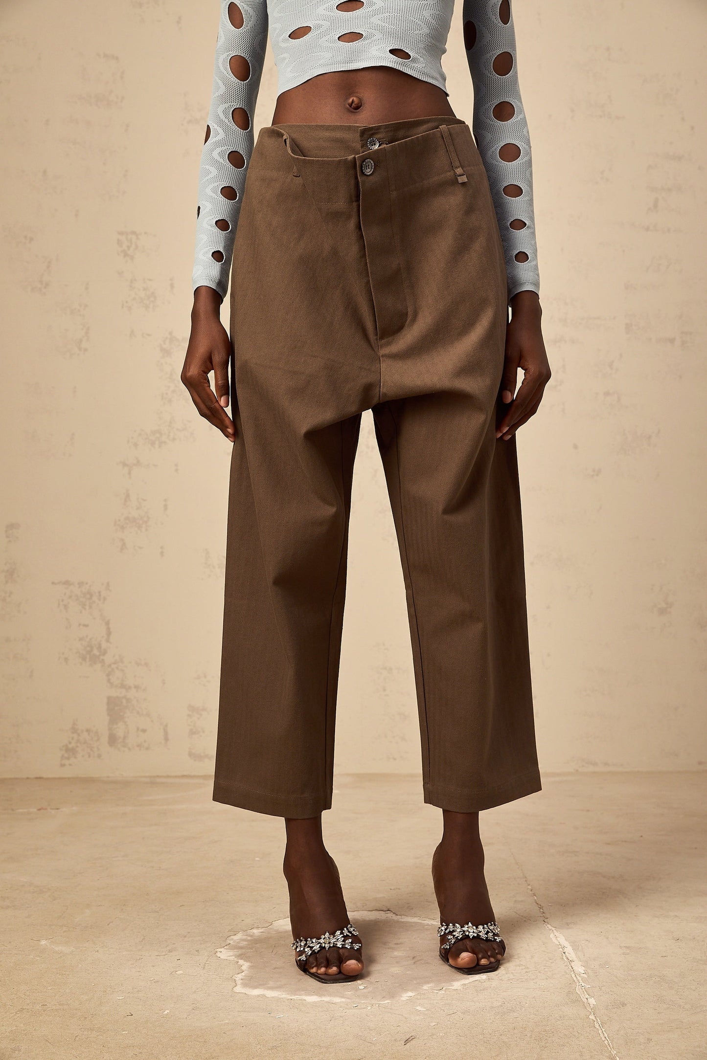 Woman wearing brown wide leg cropped trousers with shirred waistband standing against plain background