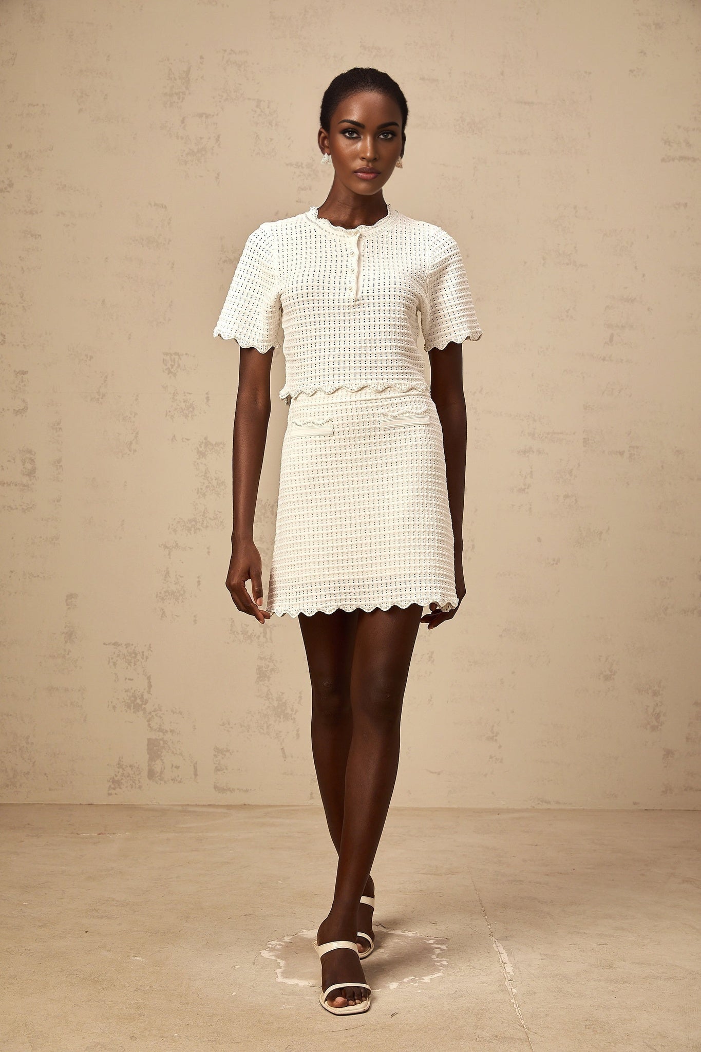 Woman wearing creamwhite matching set with ruffled top and skirt in pointelle knit fabric