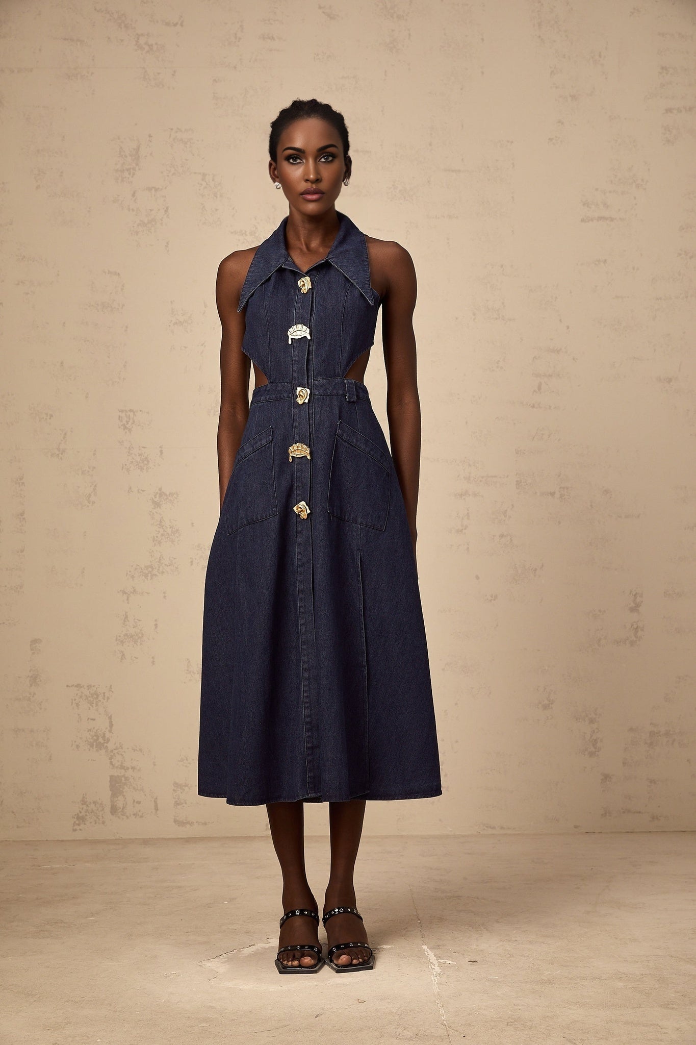 Woman wearing dark blue denim midi dress with cutout details standing against plain background