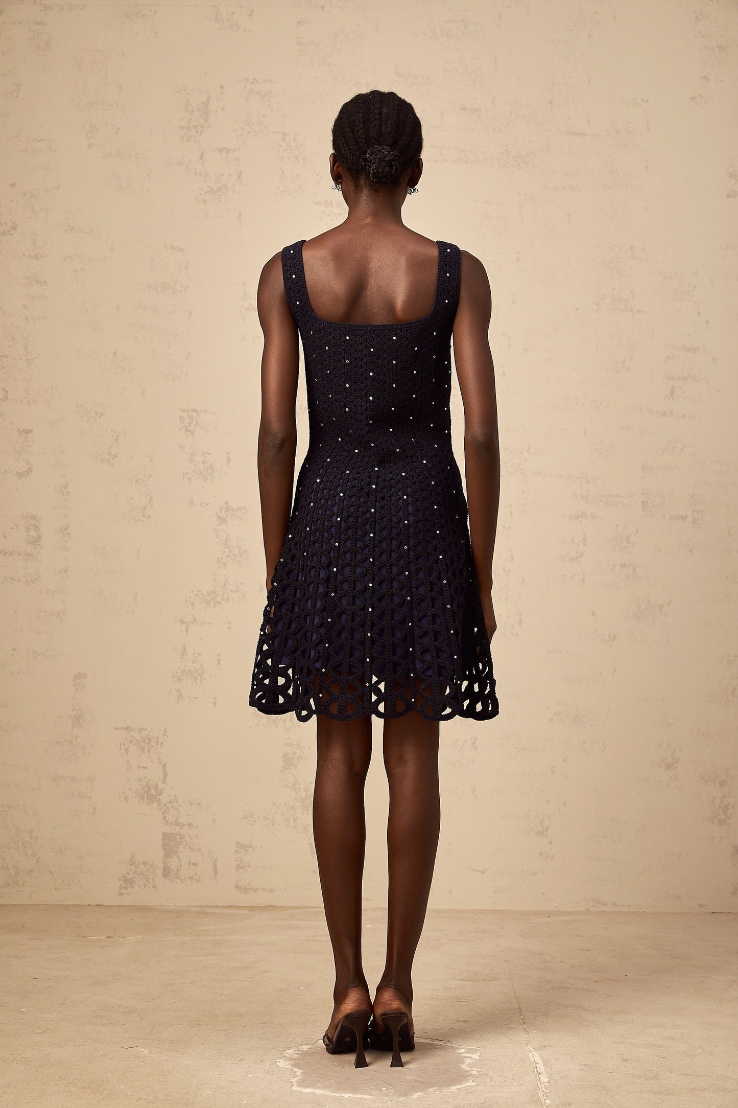 Woman wearing dark blue mini dress with crochet knit pattern and embellishments featuring cutout details