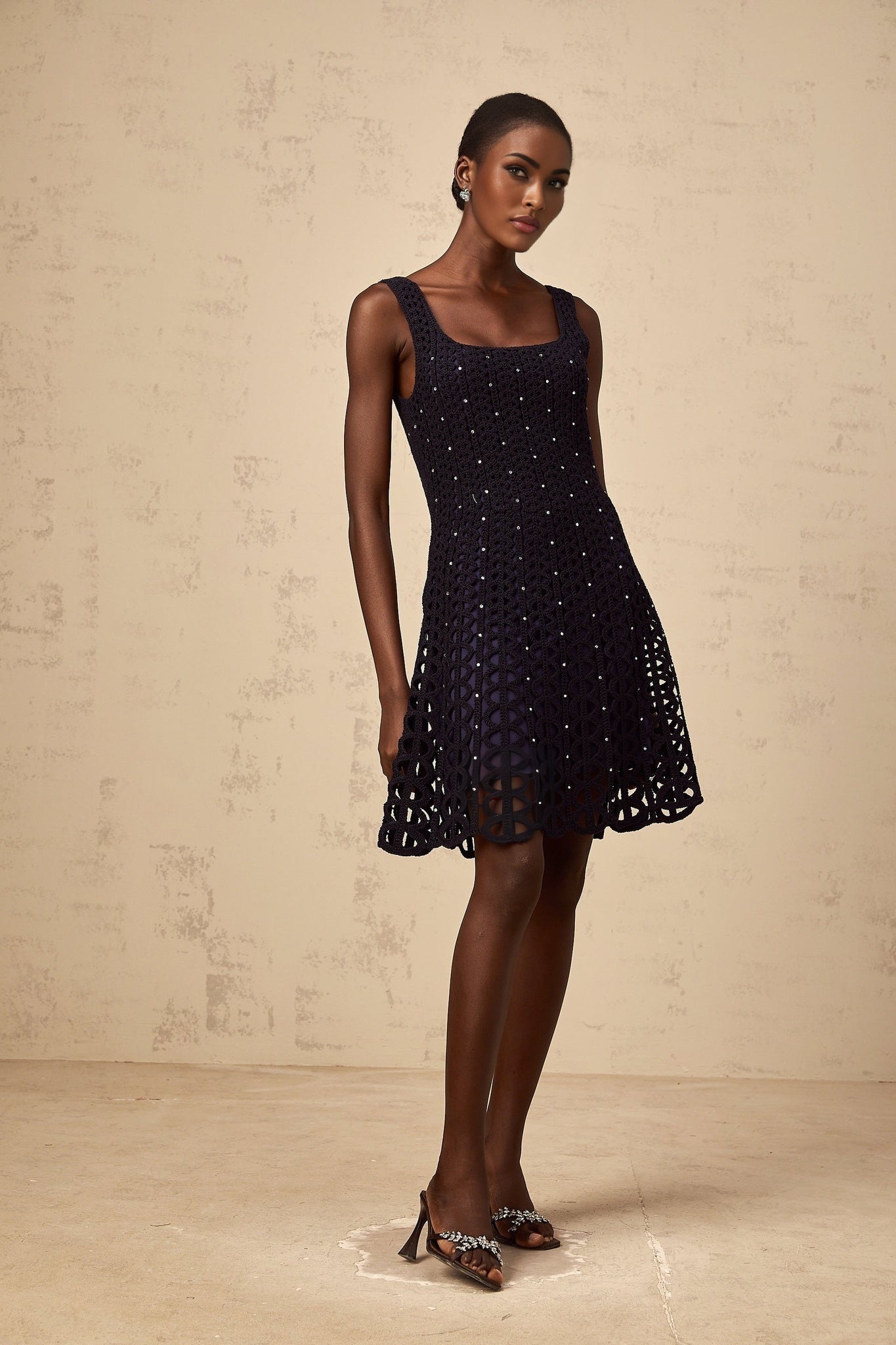 Woman wearing dark blue mini dress with crochet knit pattern and embellishments featuring cutout details
