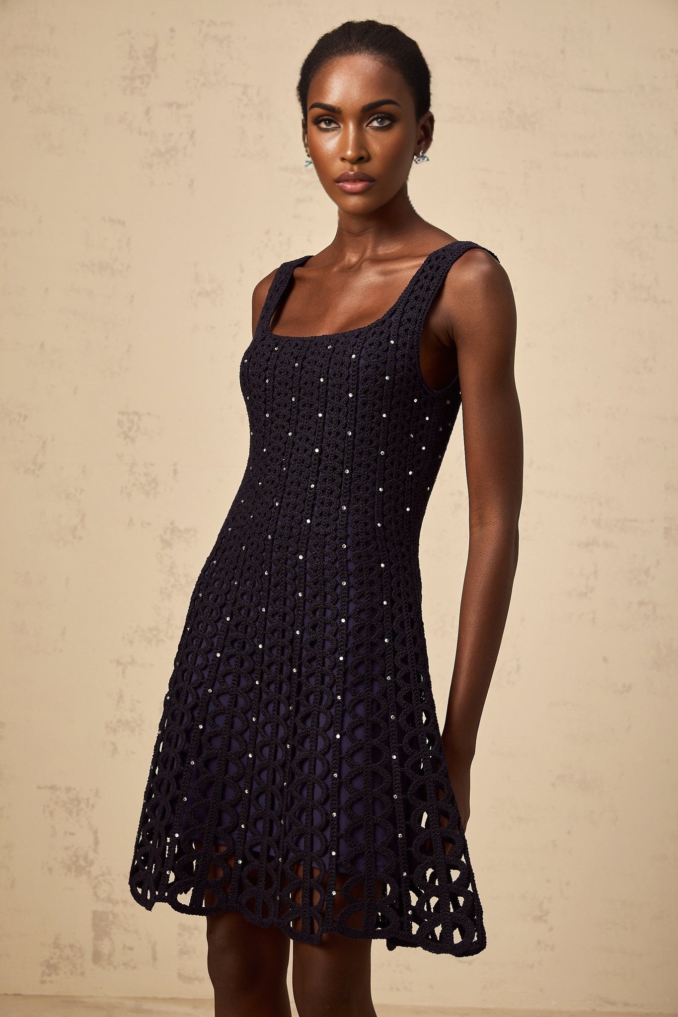 Woman wearing dark blue mini dress with embellished crochet knit pattern and cut out details