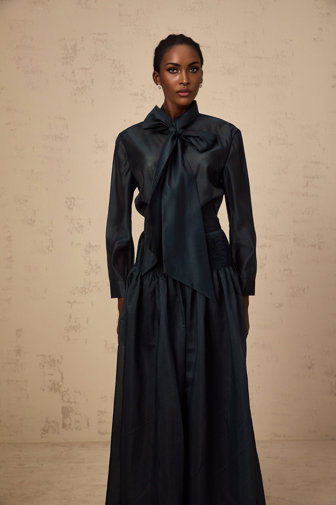 Woman wearing dark green matching set consisting of a ribbon tieneck shirt and skirt