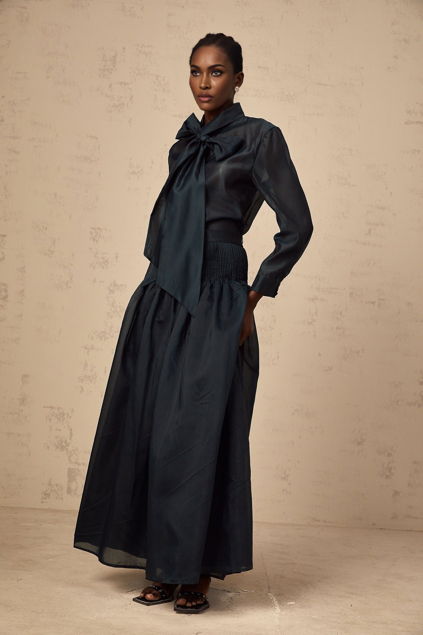 Woman wearing dark green matching set with long sleeve shirt and skirt Shirt has ribbon tie neck detail